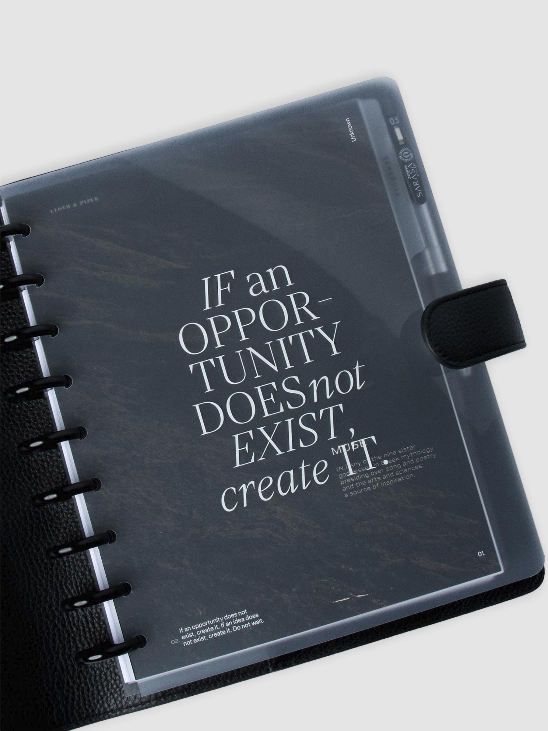 Glass Plastic Discbound Notebook Cover in Opportunity design styled inside a black leather agenda cover. The cover is used on a discbound system with black discs, layered over top of the Muse Dashboard.