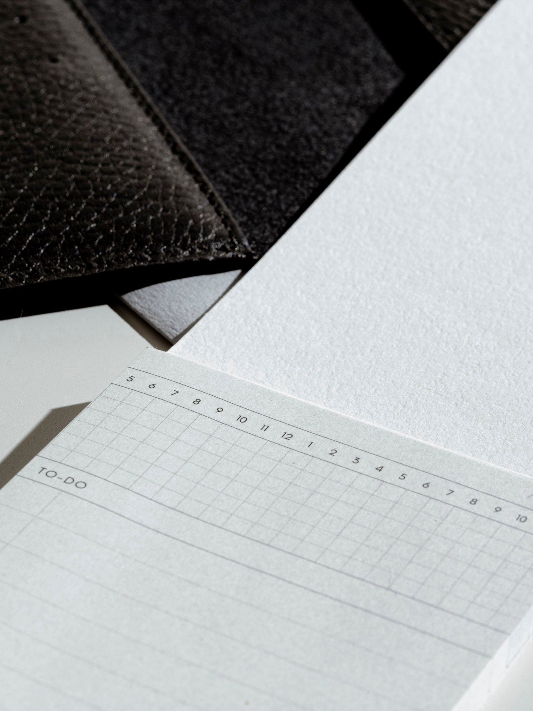 Sticky note displayed with its backing next to a black leather agenda.