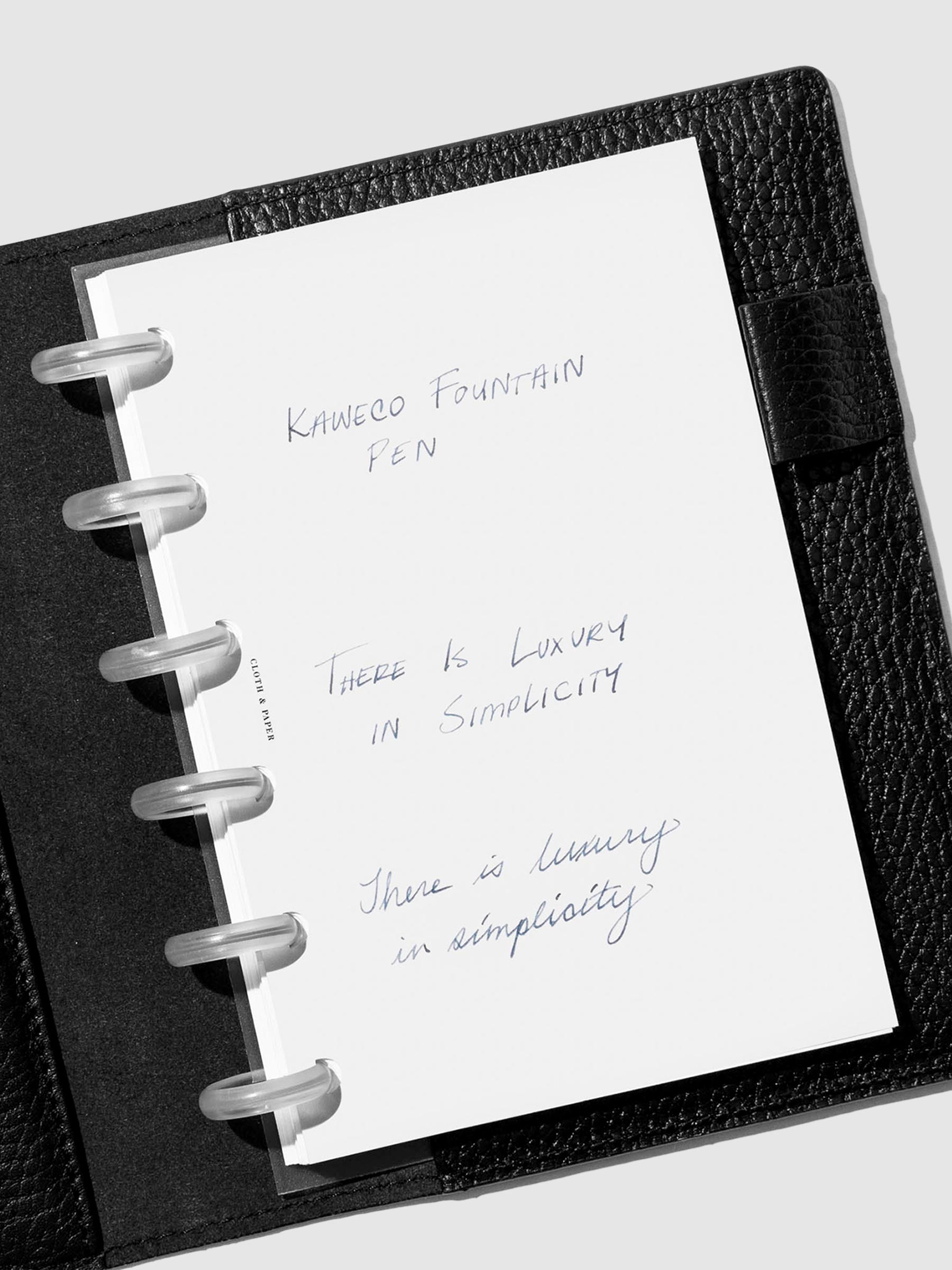 Writing sample displayed inside a black leather folio on a neutral background.