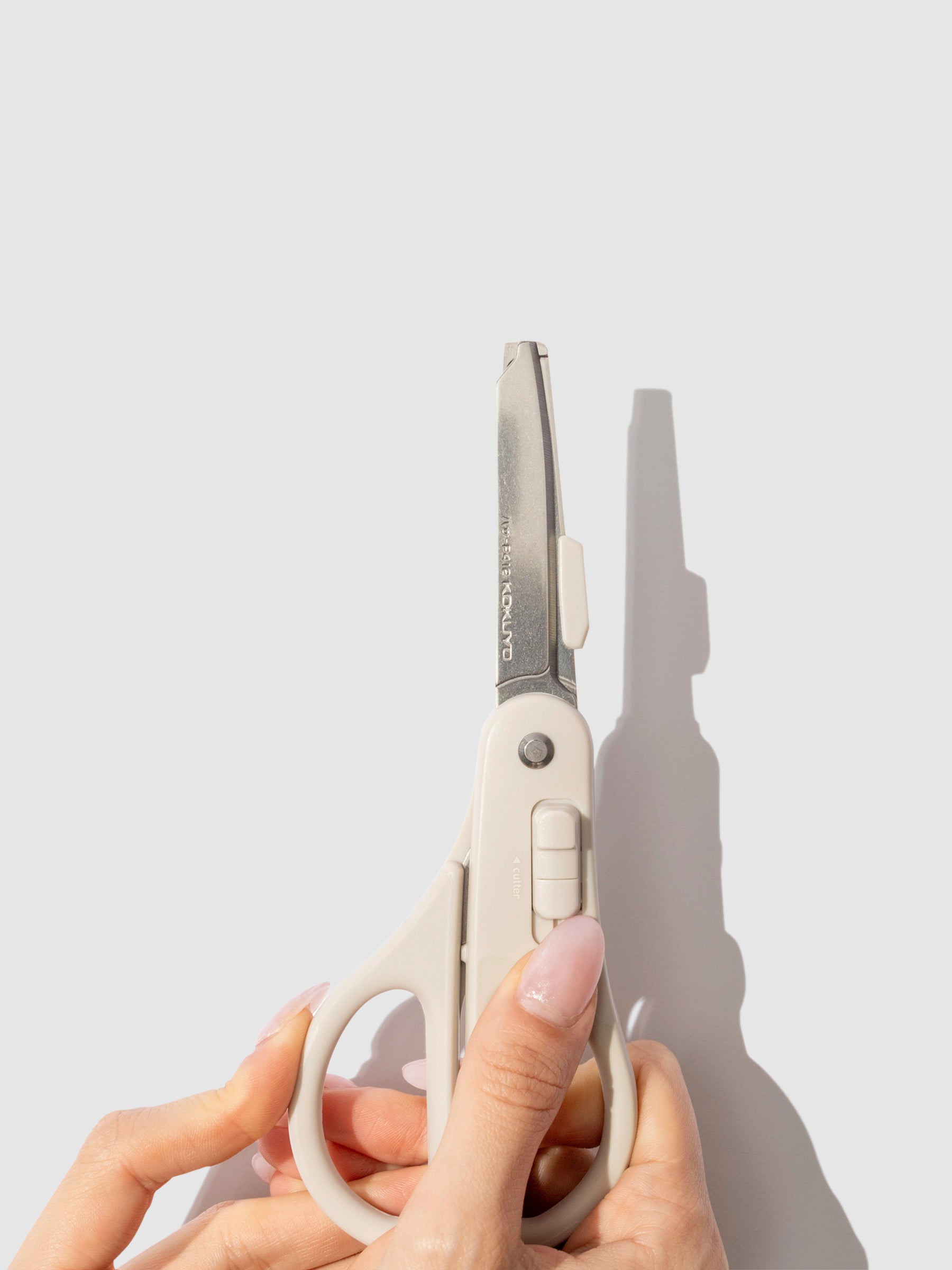 A pair of pale hands shown activating the scissors' cutting blade mode.