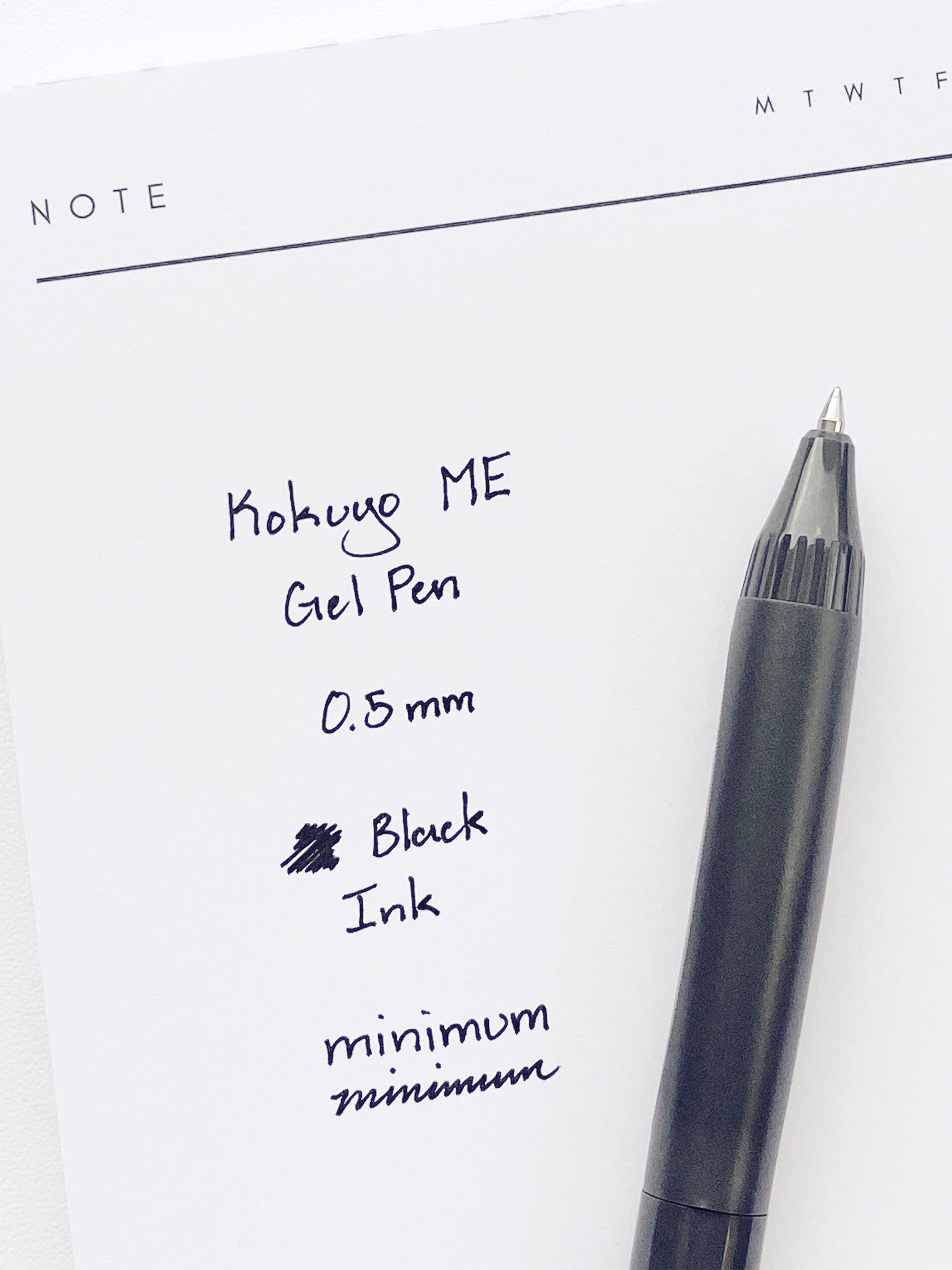 Kokuyo ME Gel Pen, Grayish Black, Cloth and Paper. Pen resting on pen test sheet displaying writing sample.