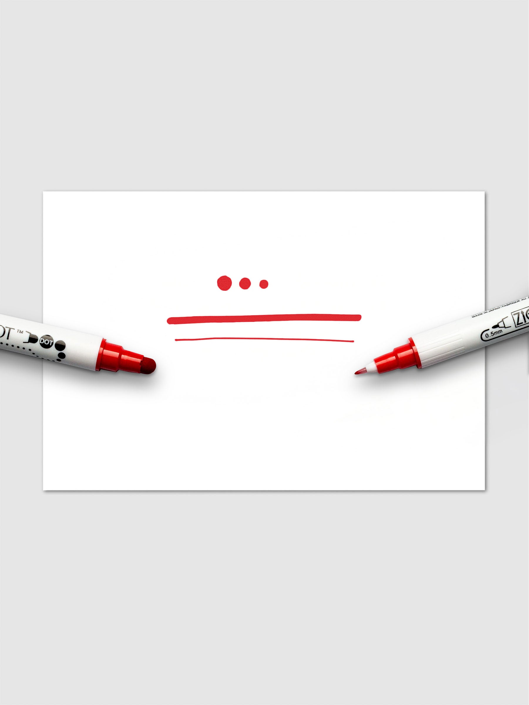 Red Kuretake ZIG Clean Color Dot Dual Tip Marker in use on white paper, showing fine lines and bold dots created by both tips.