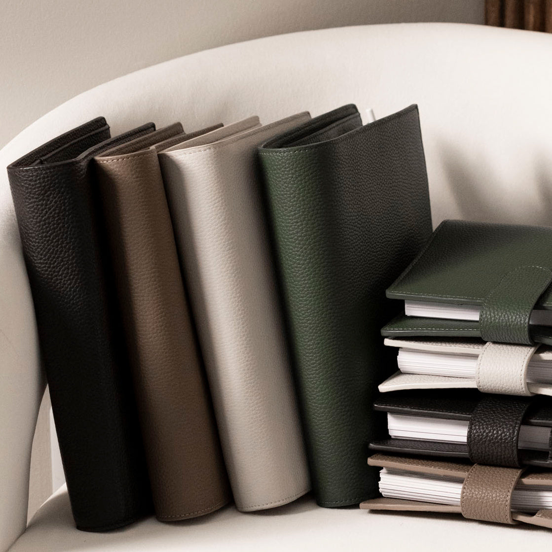 Several Foundations Leather 6-Ring Agendas are arranged side by side and stacked on a white chair.