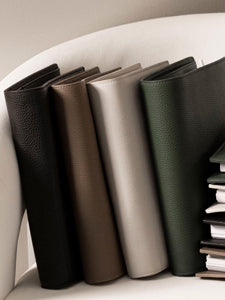 Several Foundations Leather Agendas in black, brown, beige, and green sitting in a white chair.