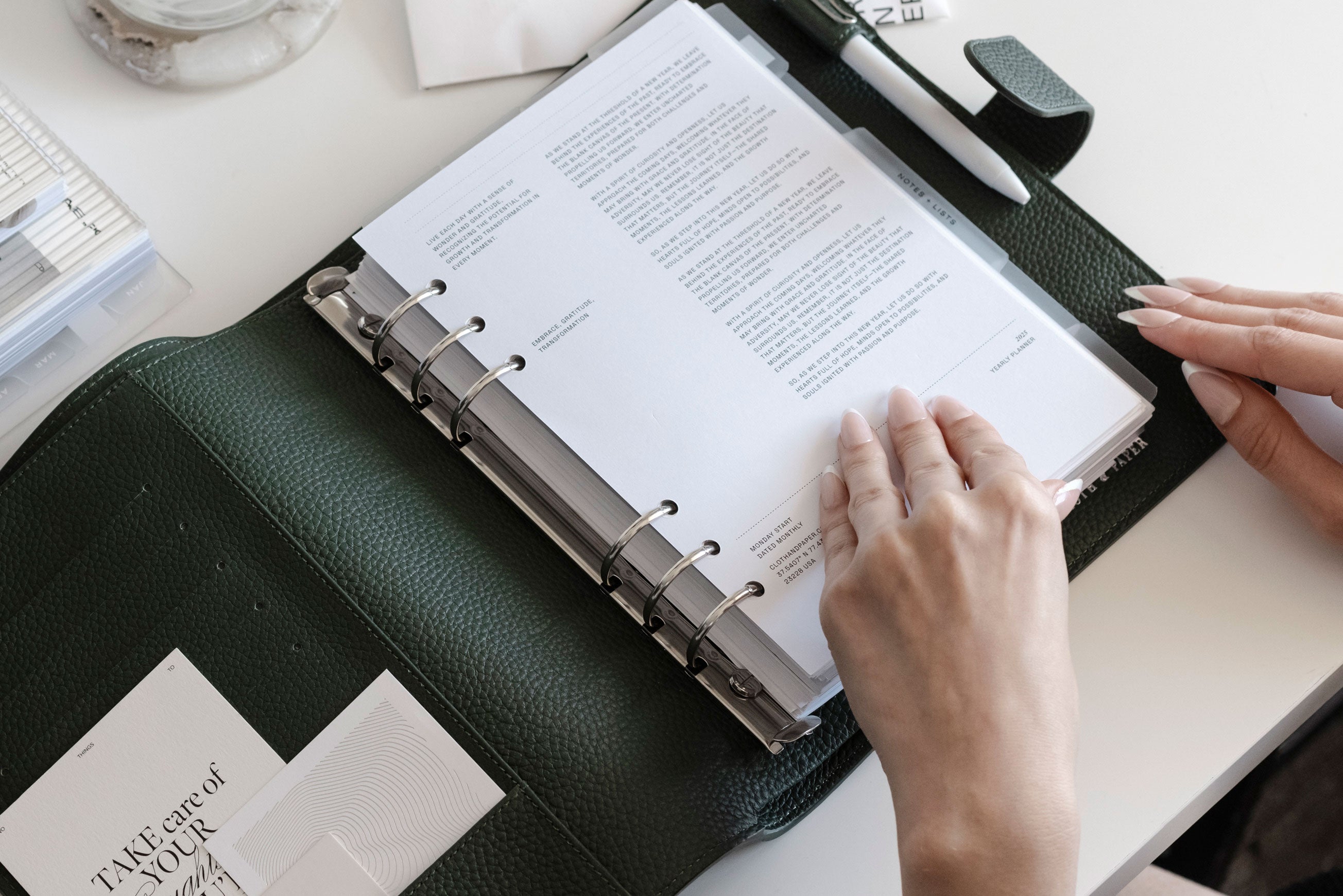 A Foundations Leather 6-Ring Agenda in A5 is opened on a white desk. Two hands are beginning to flip through the pages inside.
