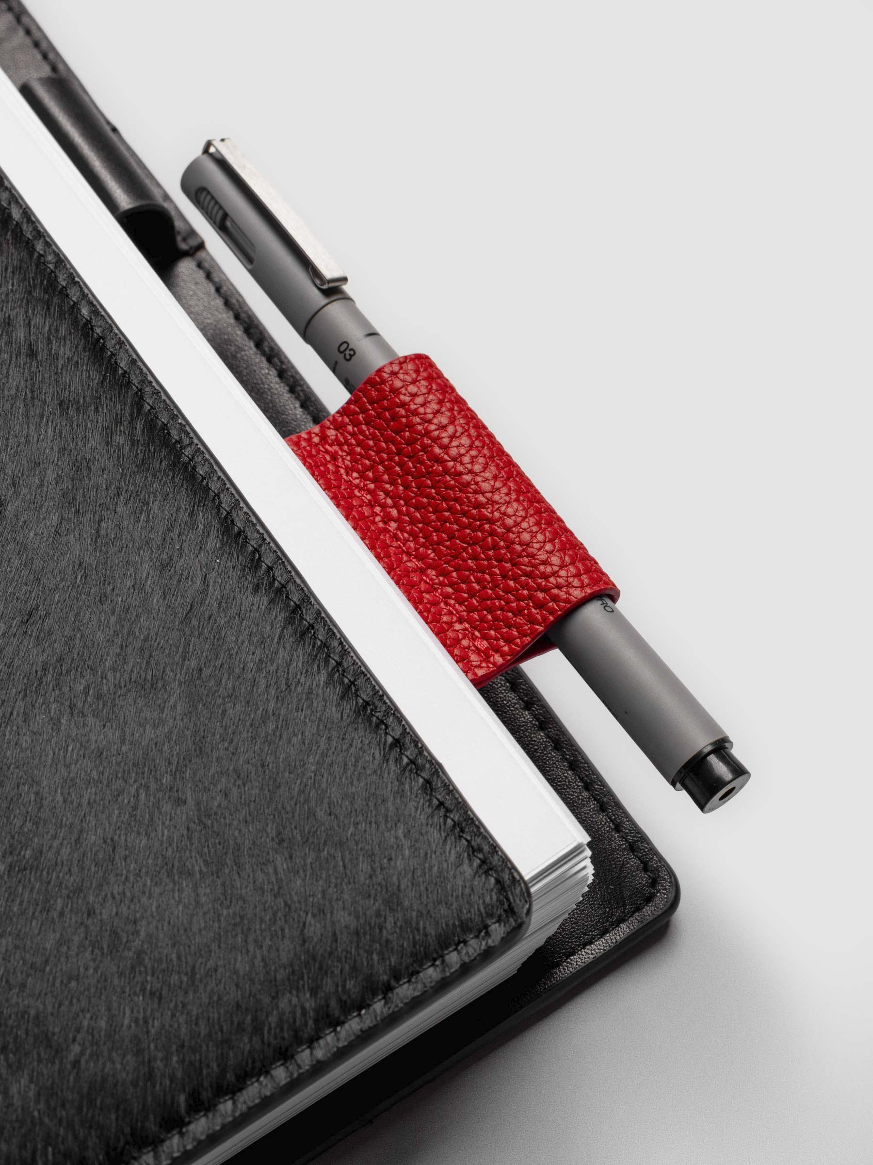Rouge clip in use inside a black leather planner. A Uni Pin Marking Pen is placed inside the pen clip.