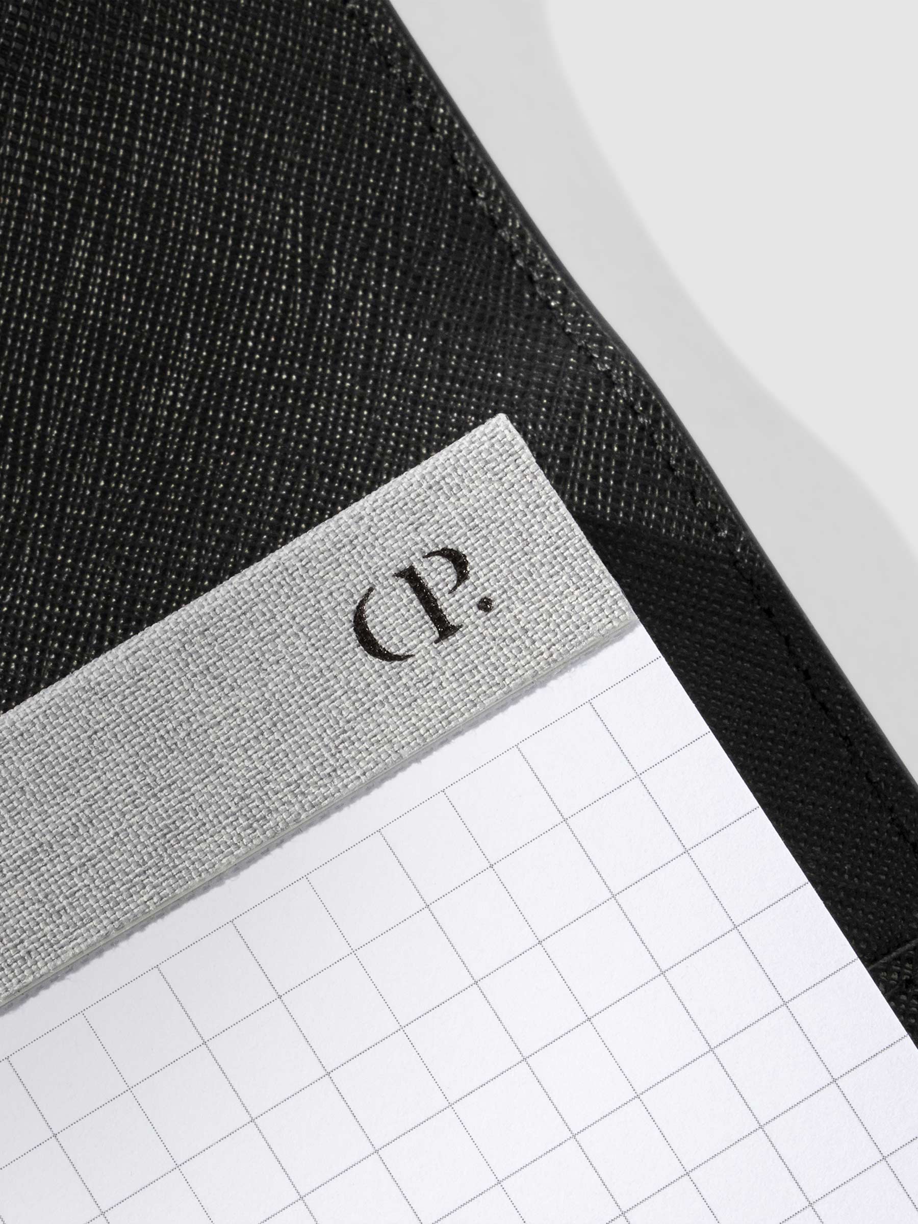 Closeup of Cloth and Paper "CP" logo printed on the fabric spine of the notepad.