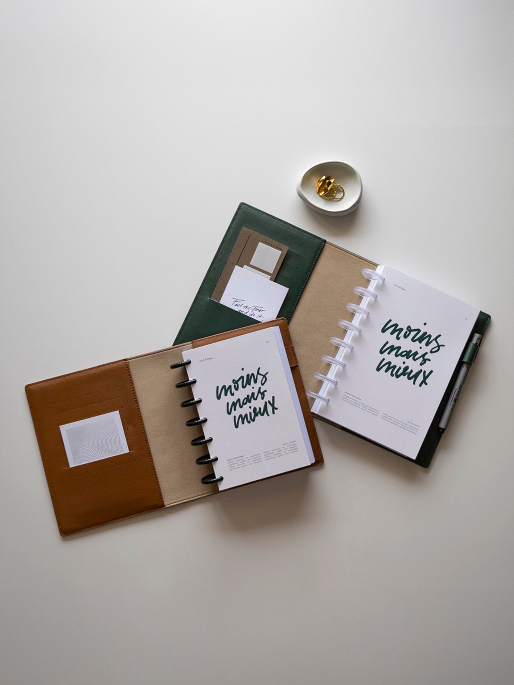 Flat lay of two stylish leather-bound disc planners with French text 'moins mais mieux' on the covers, placed on a neutral background.