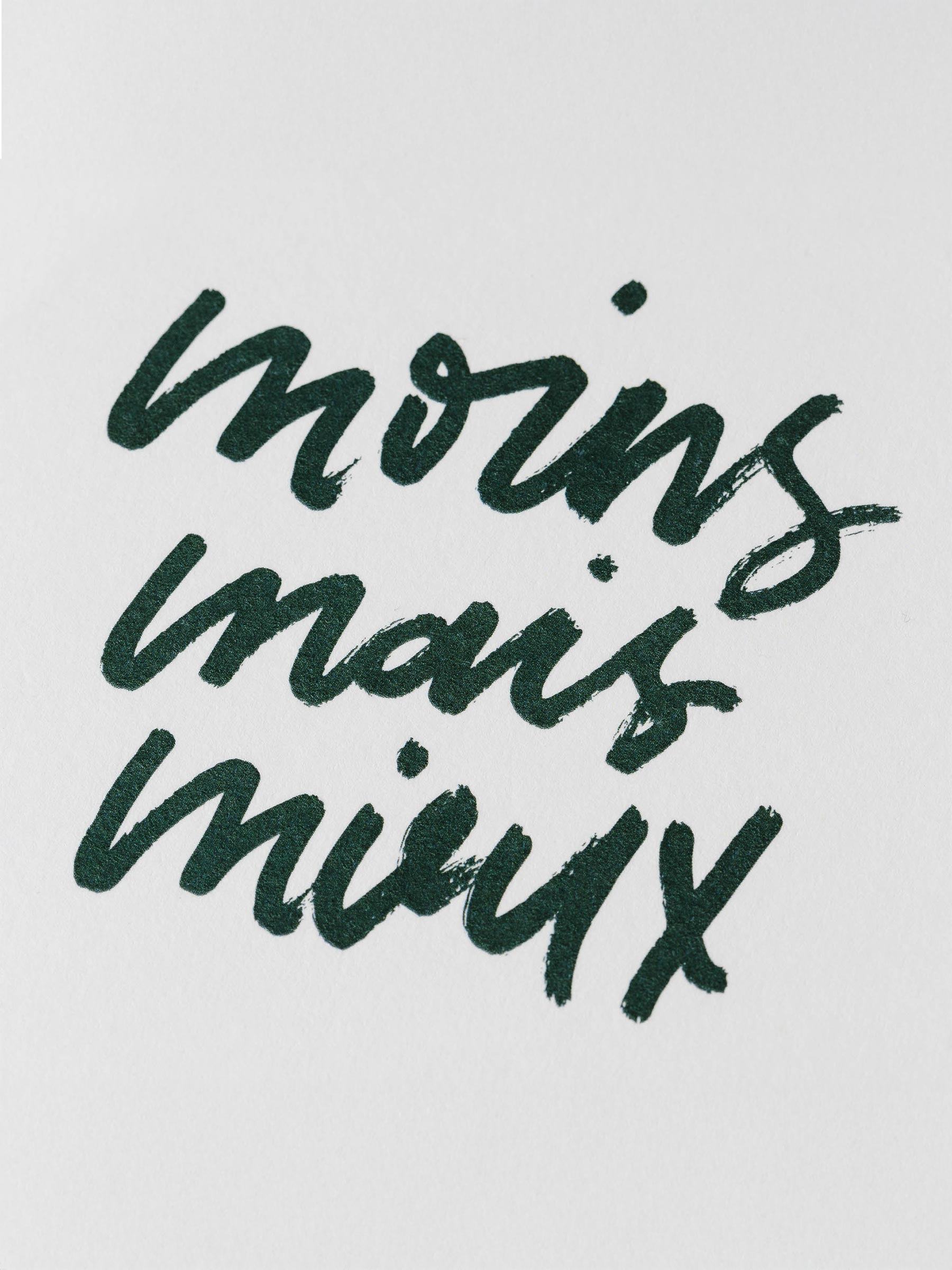 Closeup of dark green printed text that reads "moins mais mieux" in script handwriting.