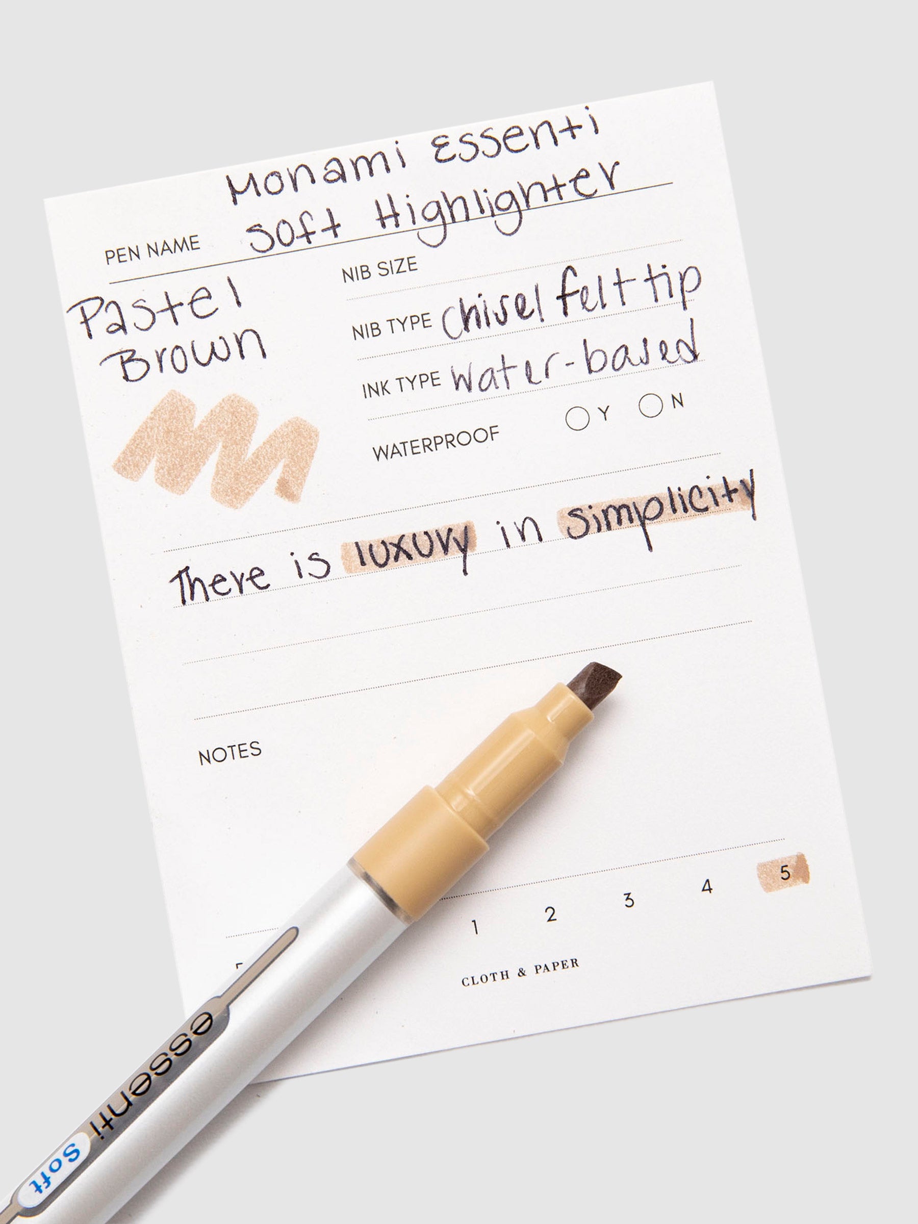 Monami Essenti Soft Highlighter, Pastel Brown, Cloth and Paper. Highlighter resting on pen test sheet displaying writing sample.