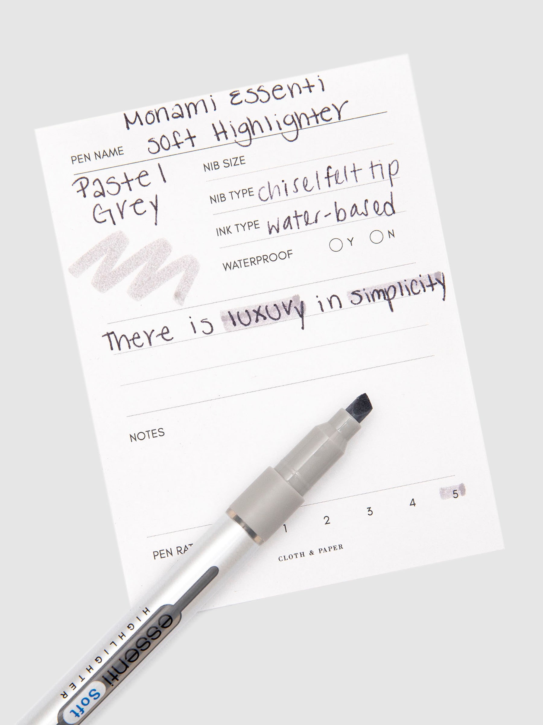 Monami Essenti Soft Highlighter | Pastel Grey | Cloth and Paper. Highlighter resting on pen test sheet displaying writing sample.