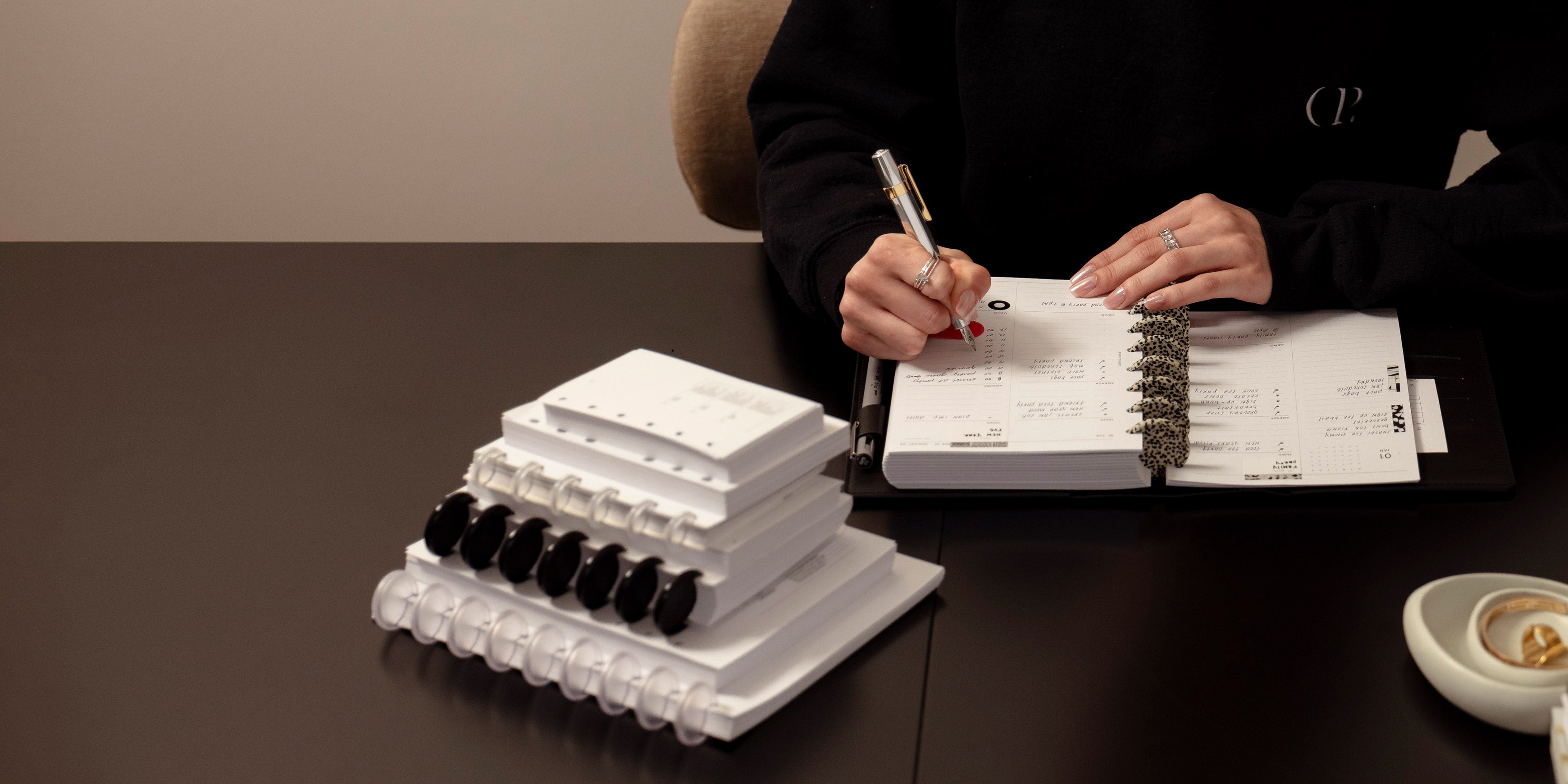 A stack of Discbound Planners and Planner Inserts. To the right are hands of a woman who is working in an open and assembled planner featuring Speckled Planner Discs.