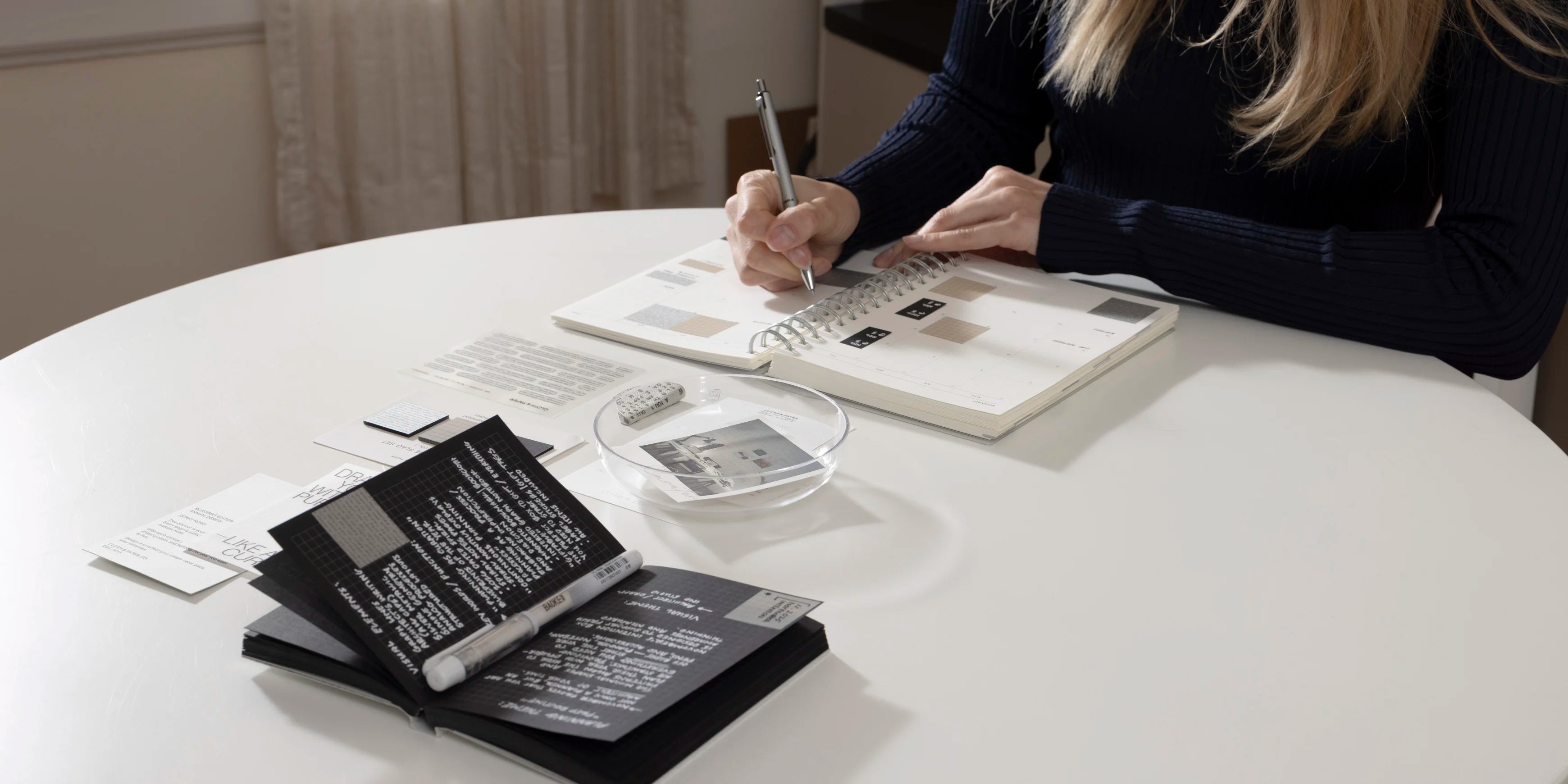 Person writing on a 2026 Spiral Notebook with stationery items on a table.