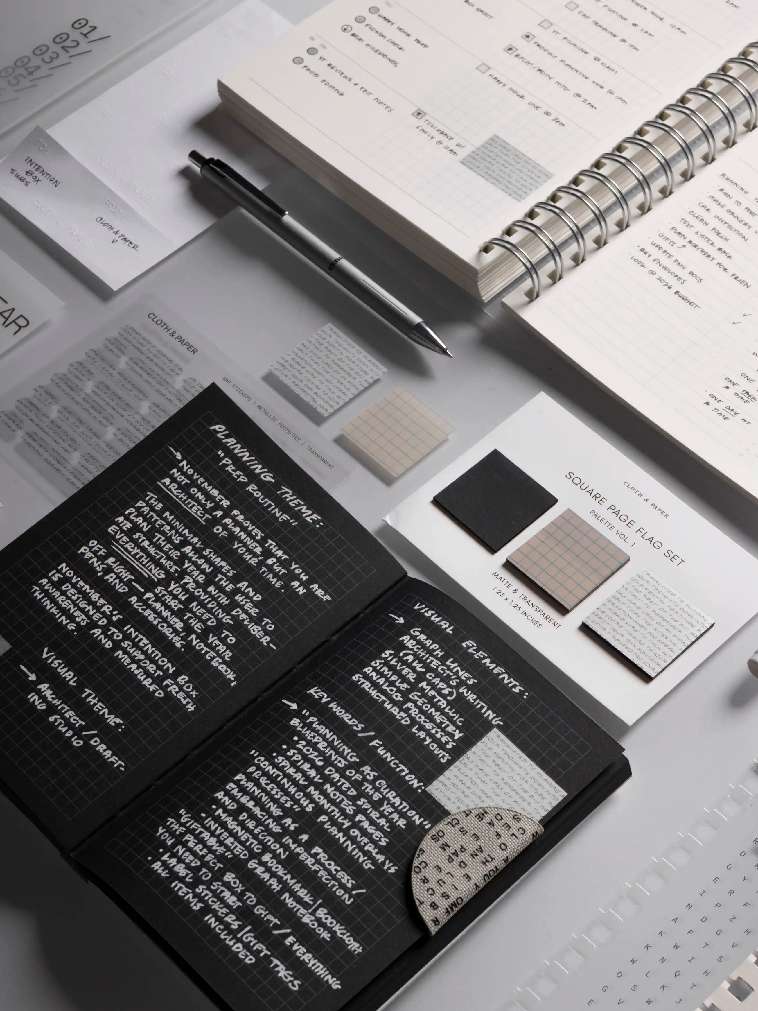 Inverted Notebook, Zebra pen, Square Page Flags, an opened 2026 Spiral Notebook and other planning accessories on a gray surface.