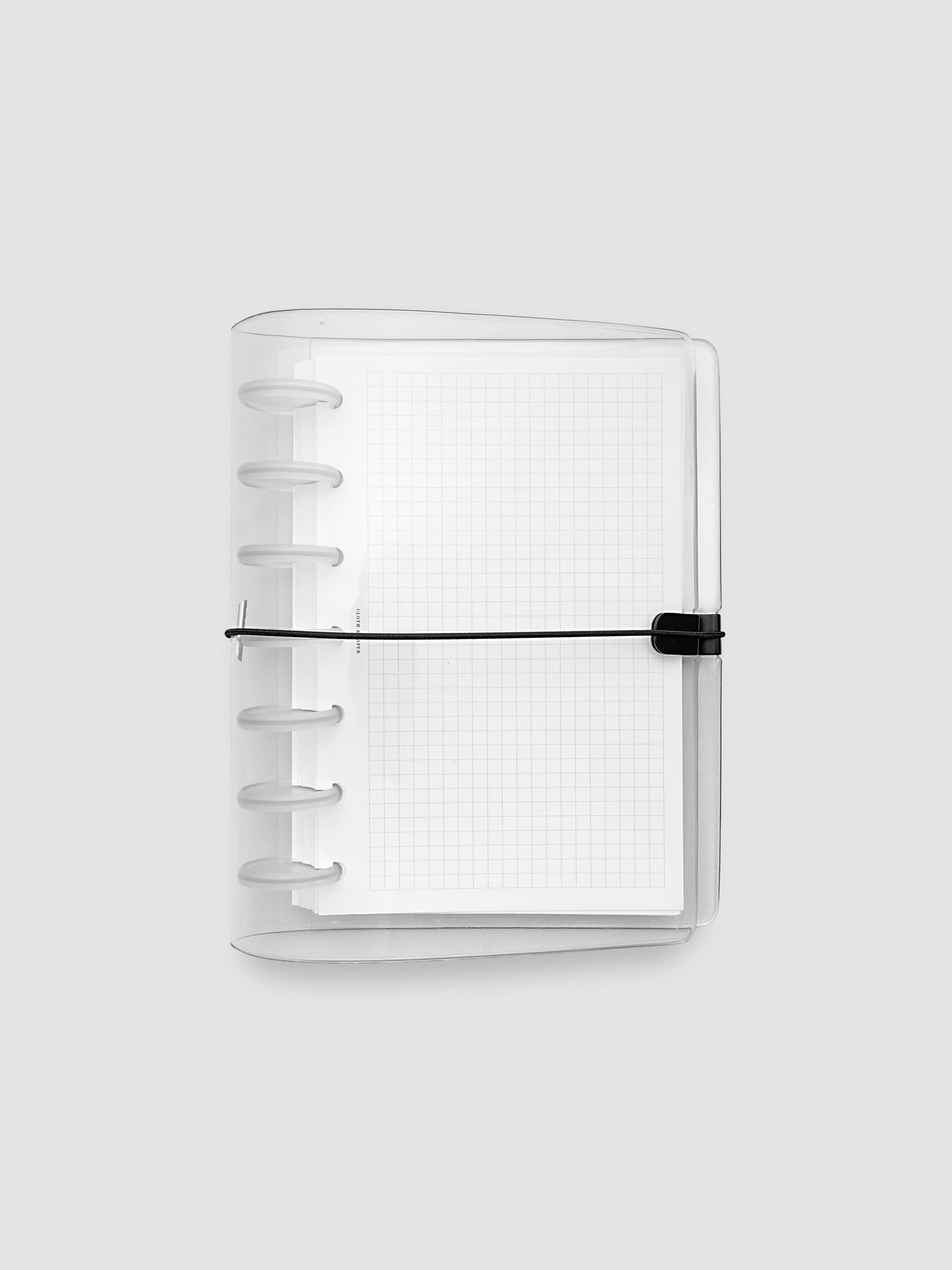 A clear plastic notebook cover with a black elastic closure band, with a discbound planner and grid inserts inside, against a light gray background.