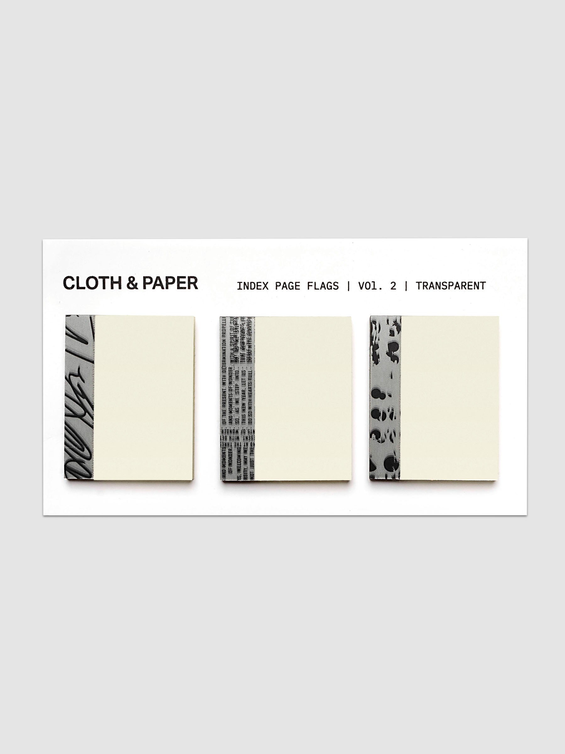 Three cream-colored index page flags with black printed text and patterned borders, displayed on a white card labeled 'CLOTH & PAPER INDEX PAGE FLAGS | VOL. 2 | TRANSPARENT' against a light gray background.