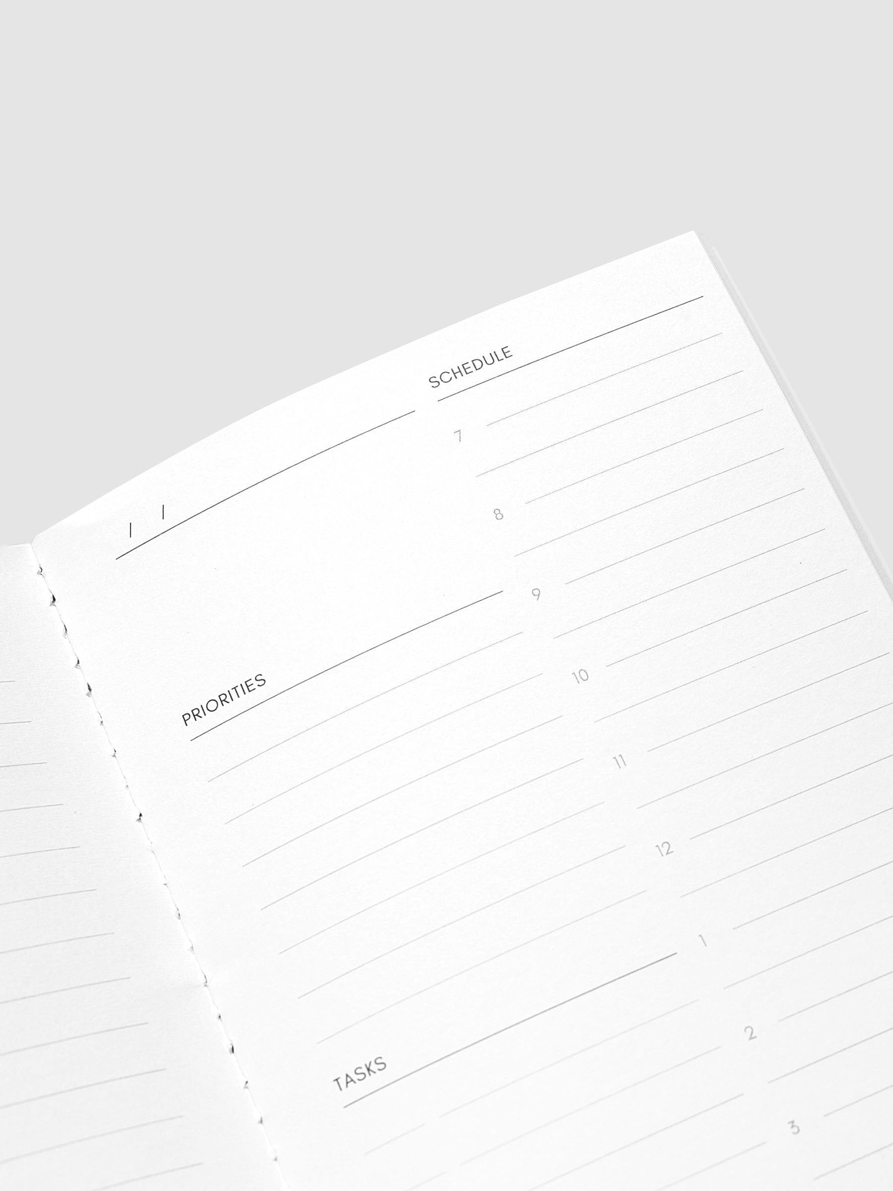 An open notebook showing lined pages with sections for schedule, priorities, and tasks on a light gray background.