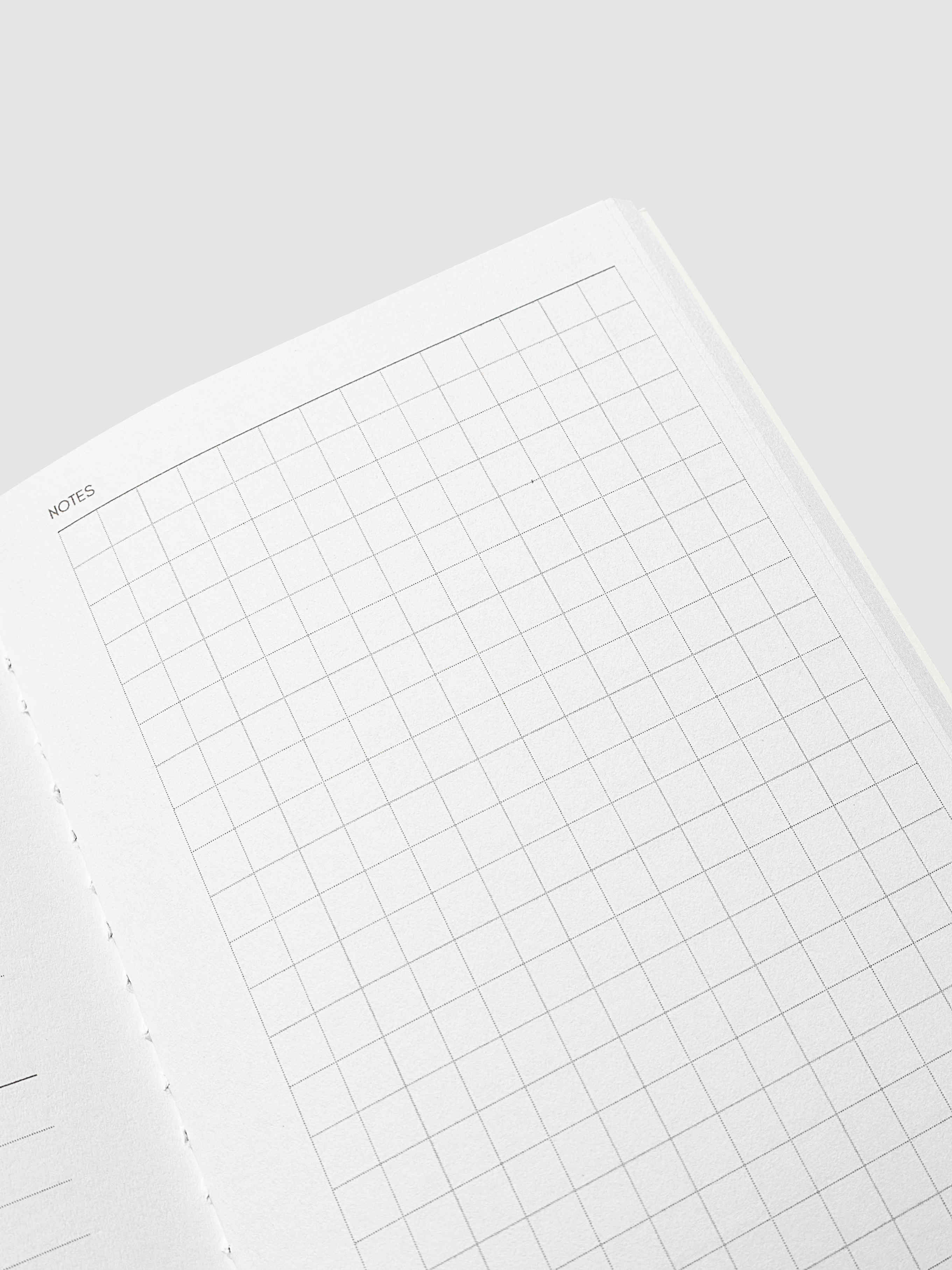 An open notebook or planner showing a clean white page with a light gray grid and a small 'NOTES' header in the upper left corner, photographed on a light gray background.