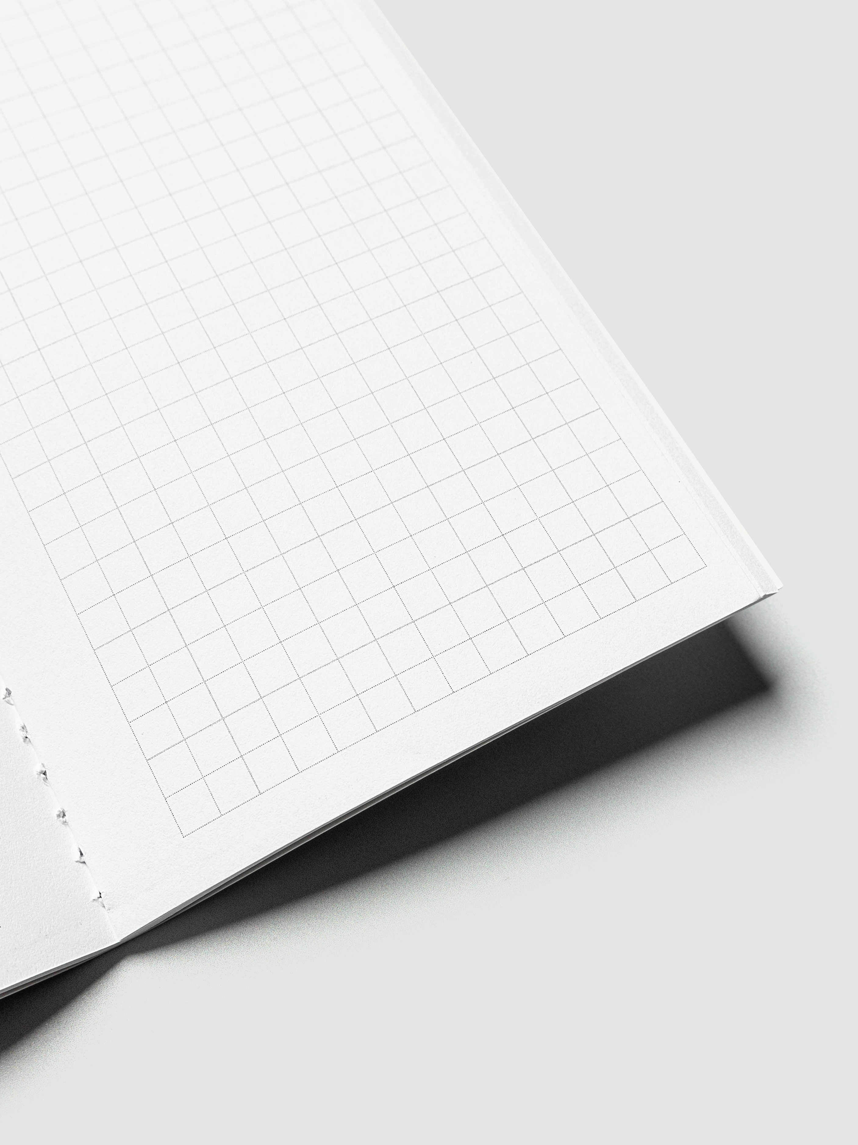 A close-up of a white grid notebook page with a thin square grid pattern, shown at an angle on a light gray background with a soft shadow.