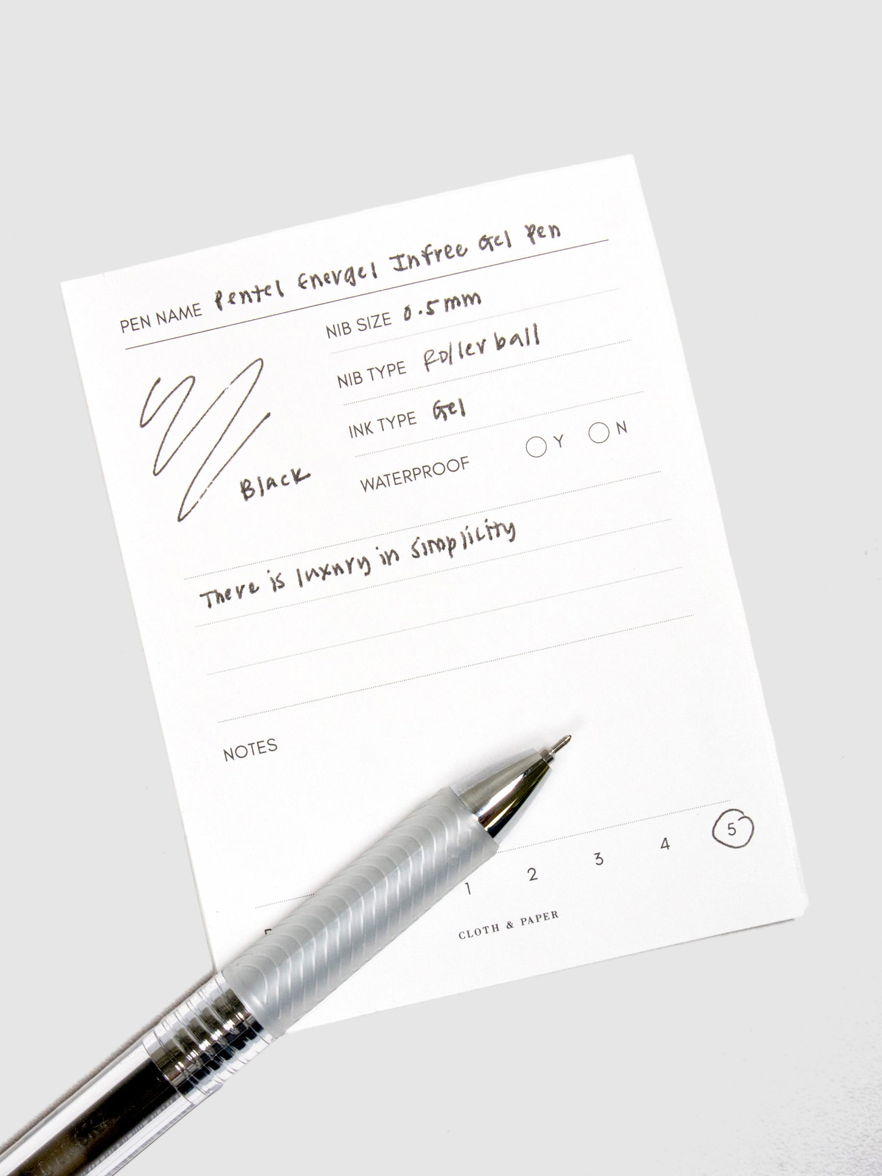 Pentel Energel Infree Gel Pen, Black, Cloth and Paper. Pen resting on pen test sheet displaying writing sample.