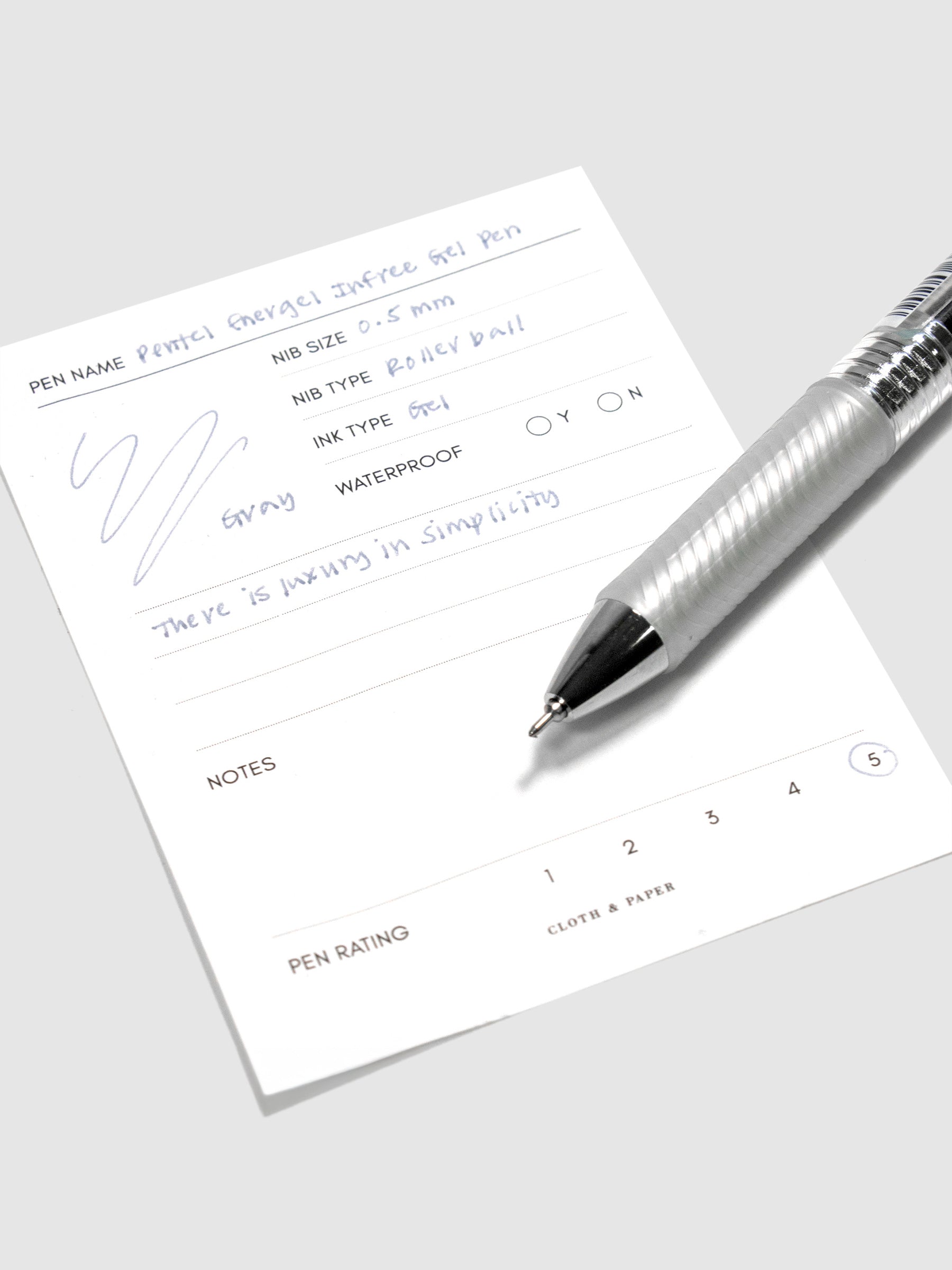 Pentel Energel Infree Gel Pen, Gray, Cloth and Paper. Pen resting on pen test sheet displaying writing sample.