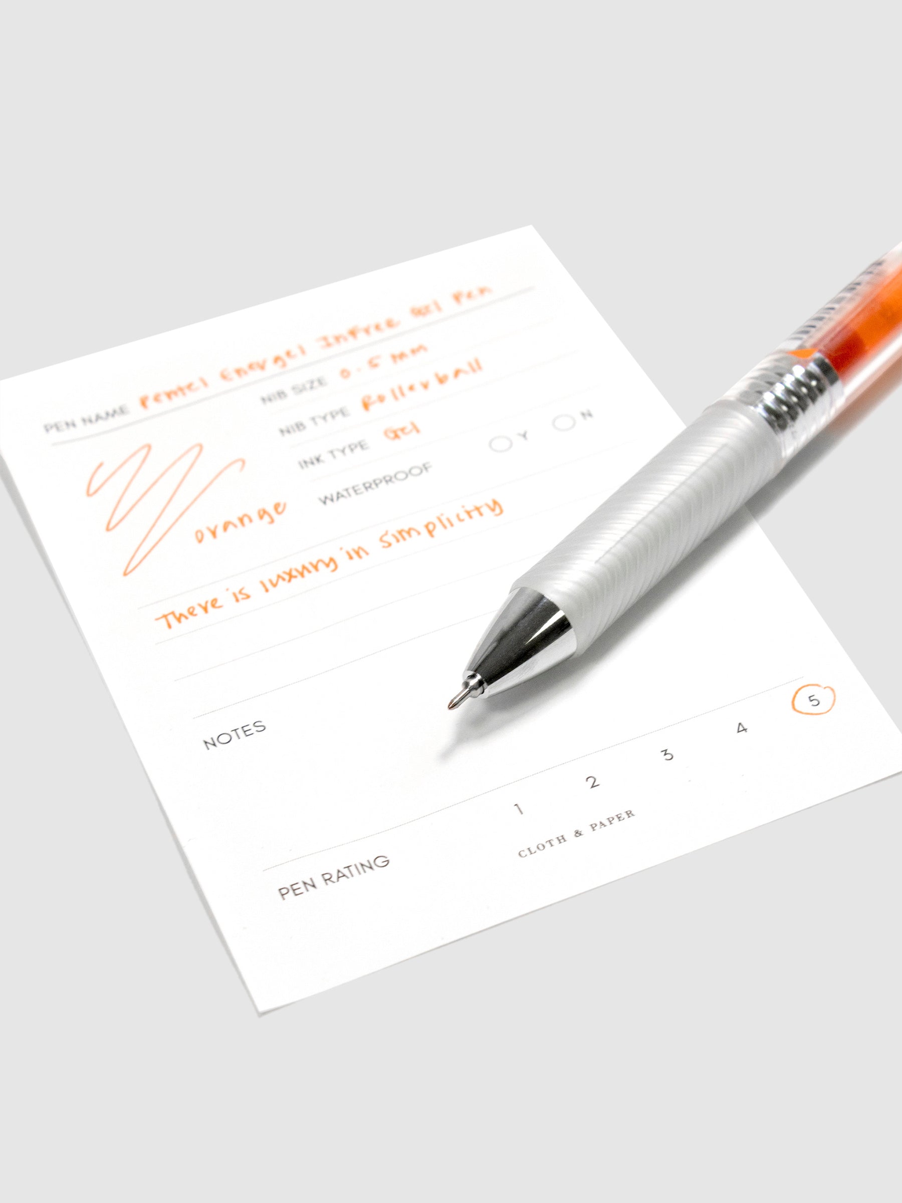 Pentel Energel Infree Gel Pen, Orange, Cloth and Paper. Pen resting on pen test sheet displaying writing sample.