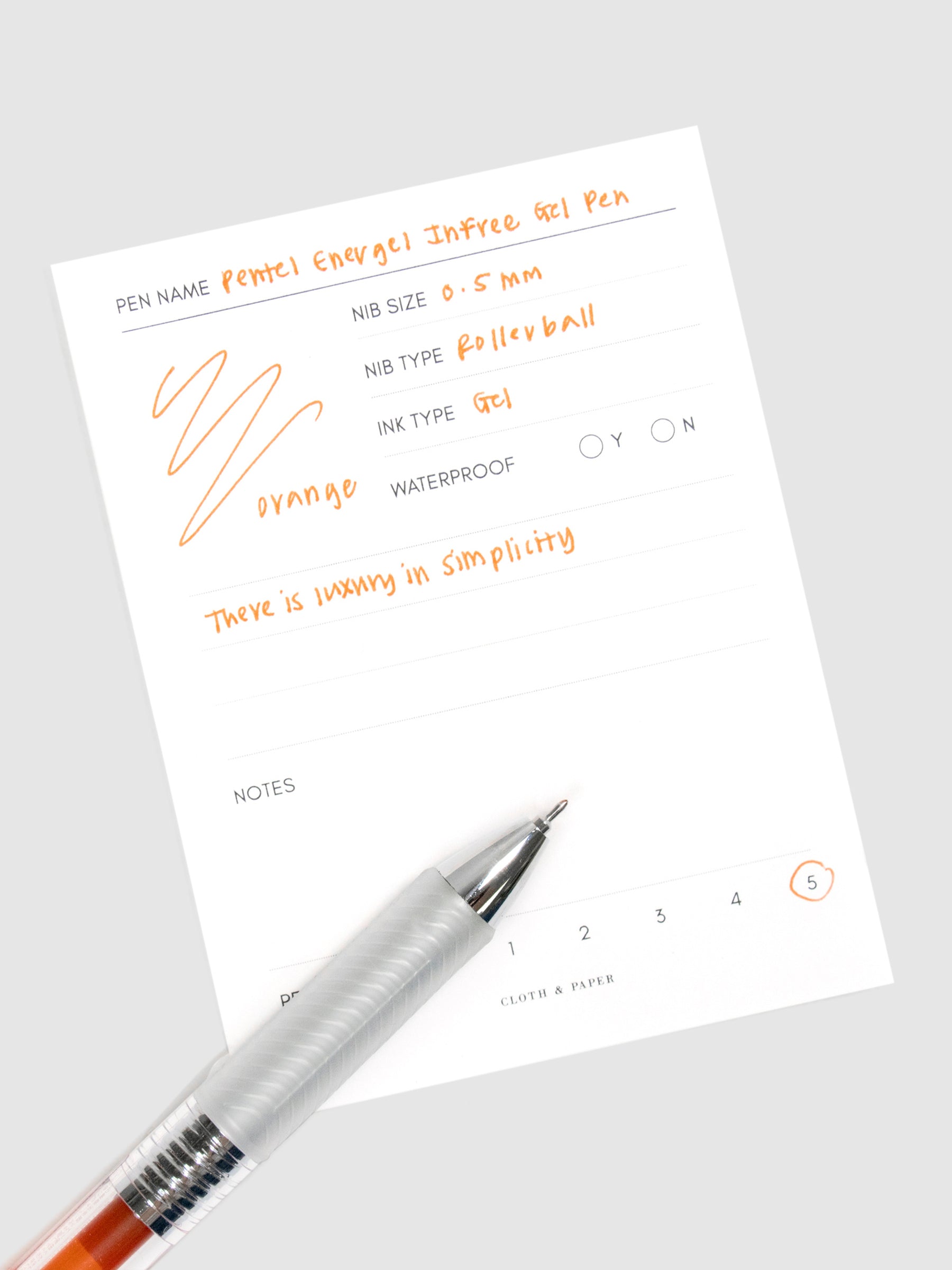 Pentel Energel Infree Gel Pen, Orange, Cloth and Paper. Close up on pen nib resting on pen test sheet.