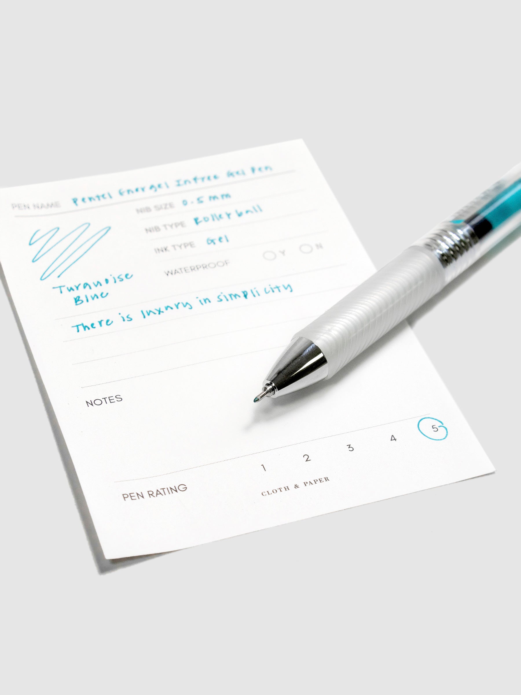 Pentel Energel Infree Gel Pen, Turquoise-Blue, Cloth and Paper. Pen resting on pen test sheet displaying writing sample.