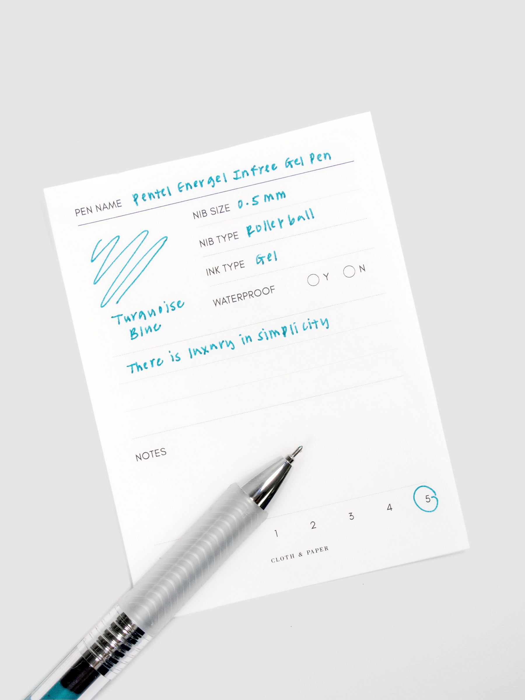 Pentel Energel Infree Gel Pen, Turquoise-Blue, Cloth and Paper. Close up on pen nib resting on pen test sheet.