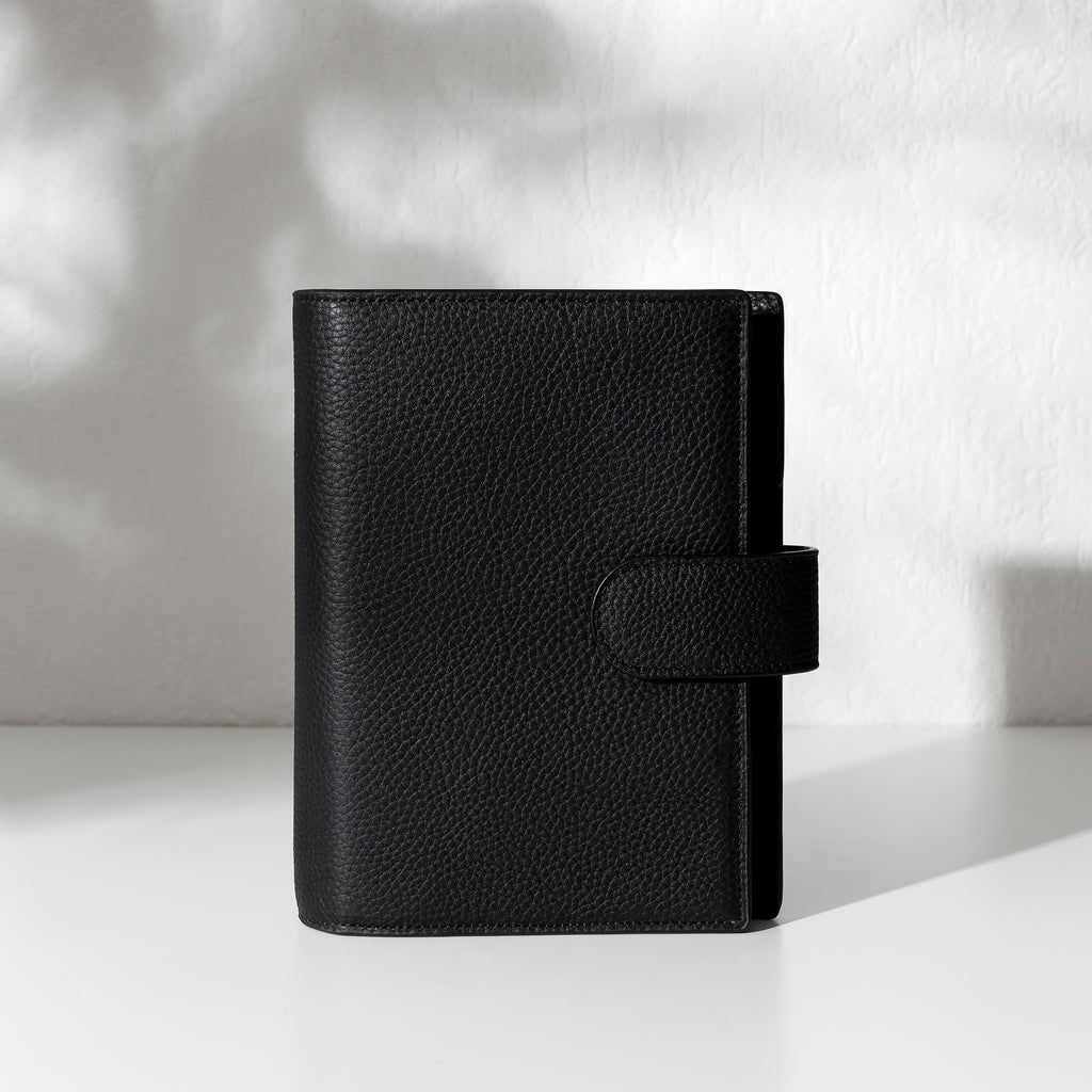 Black leather agenda displayed on an off-white background.