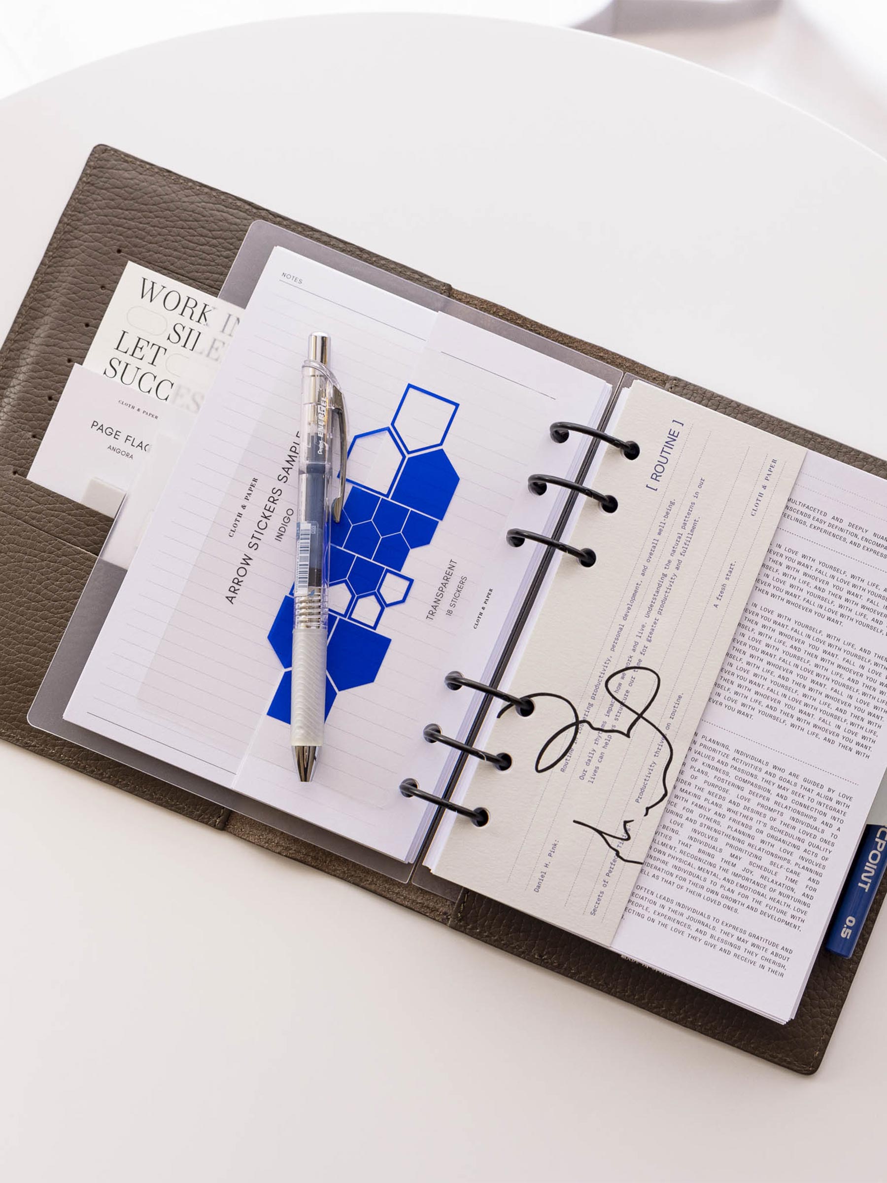 Dashboard shown in use inside a brown leather planner sitting on a white table. It is accompanied by an insert, two pens, and an indigo arrow sticker sheet.