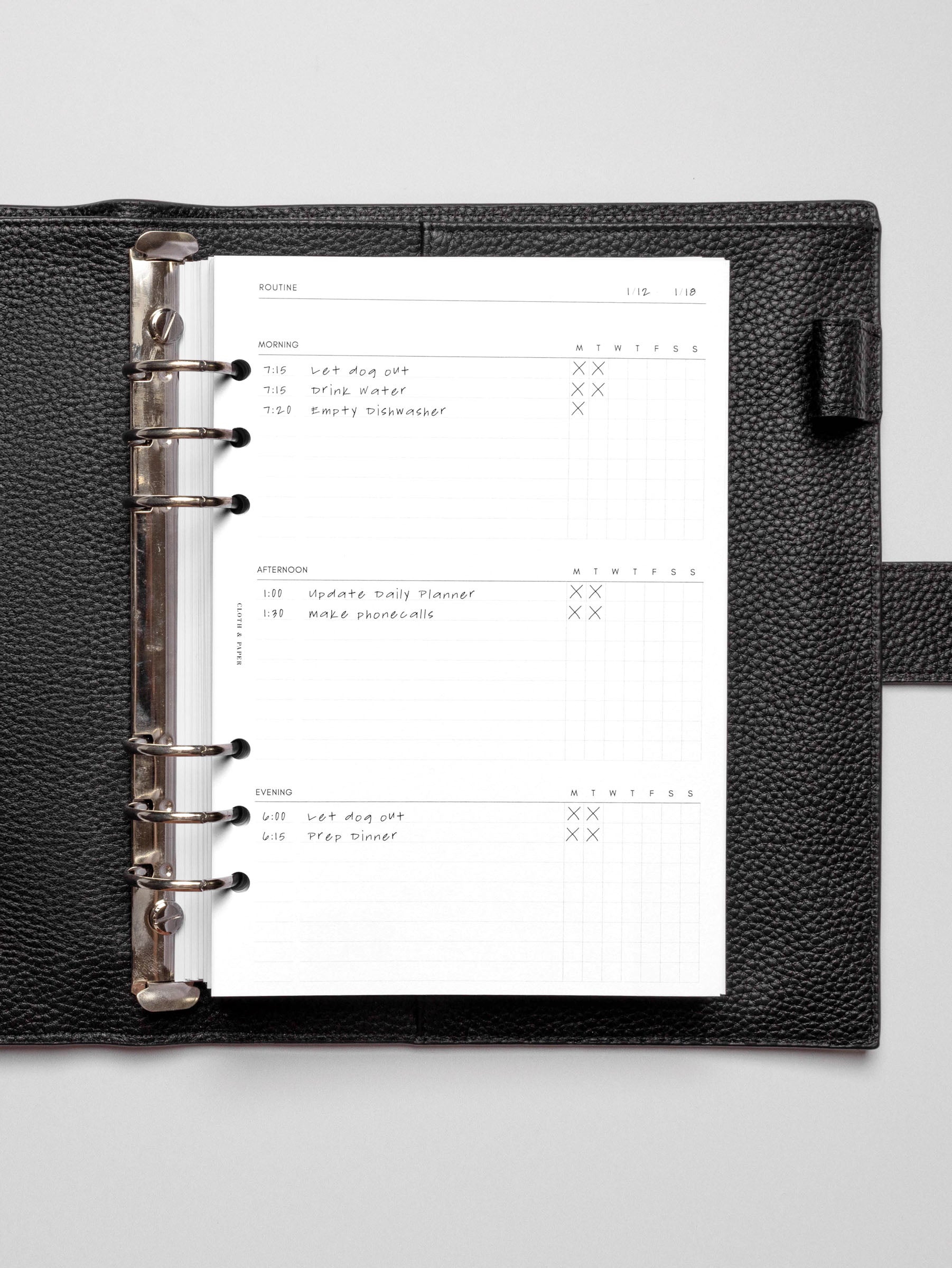 Insert in use inside a black discbound planner agenda system. Spread displays two days' worth of morning, afternoon, and evening routines.