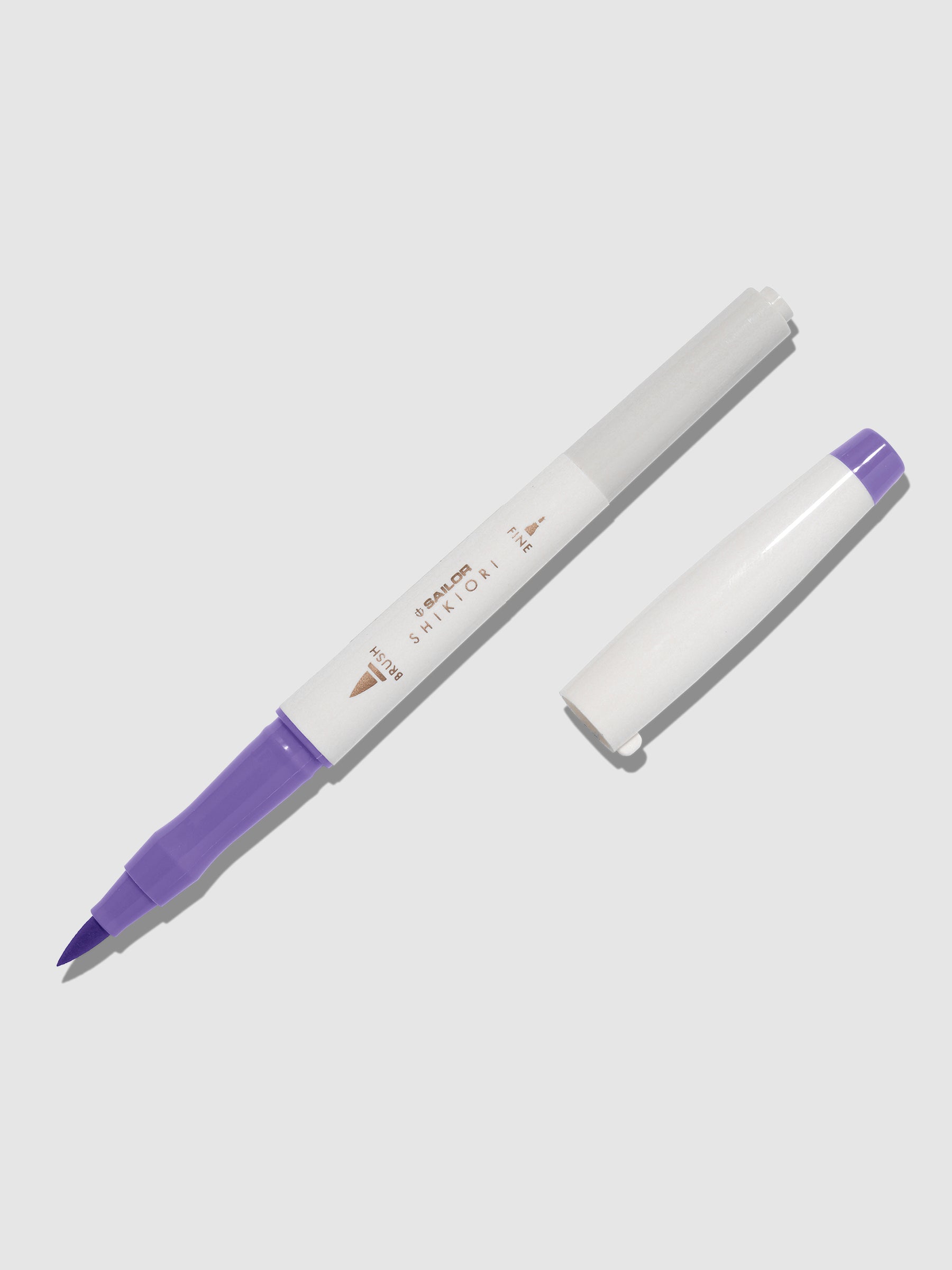 Brush pen displayed on a neutral background. It is uncapped with its brush nib exposed, and the cap lying parallel to the marker. Color pictured is Fujisugata.