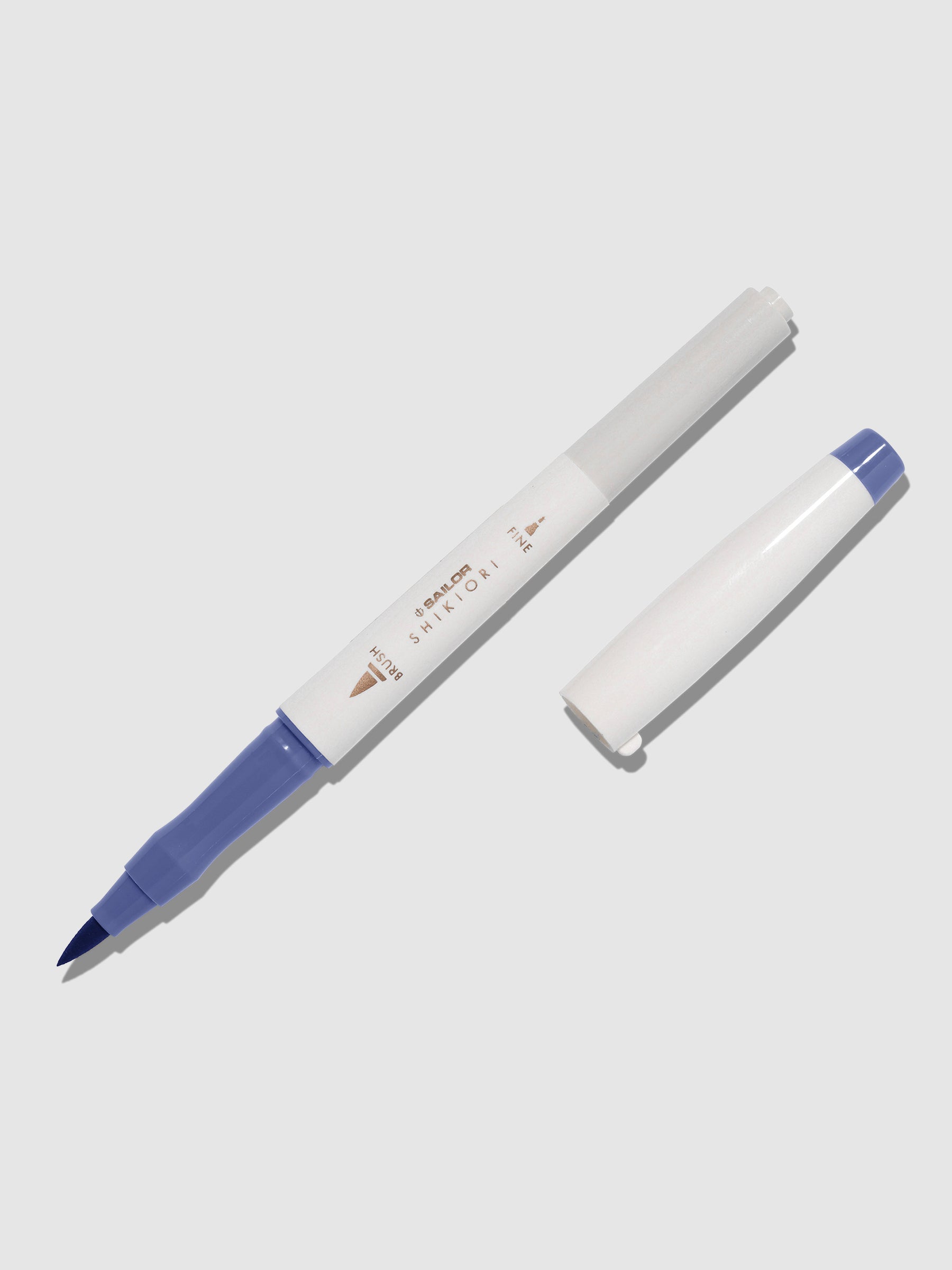 Brush pen displayed on a neutral background. It is uncapped with its brush nib exposed, and the cap lying parallel to the marker. Color pictured is Nioisumire.