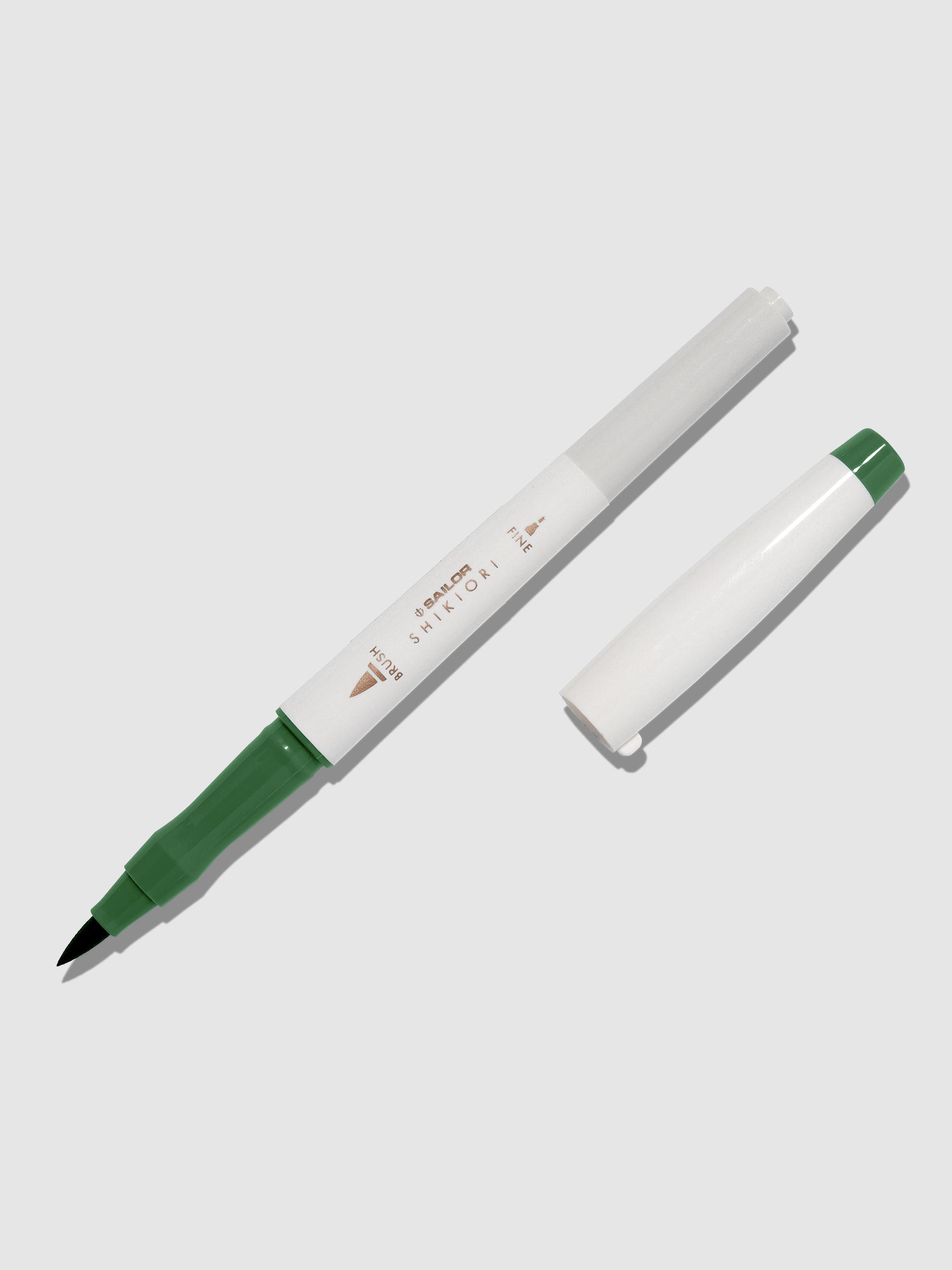 Brush pen displayed on a neutral background. It is uncapped with its brush nib exposed, and the cap lying parallel to the marker. Color pictured is Tokiwamatsu.
