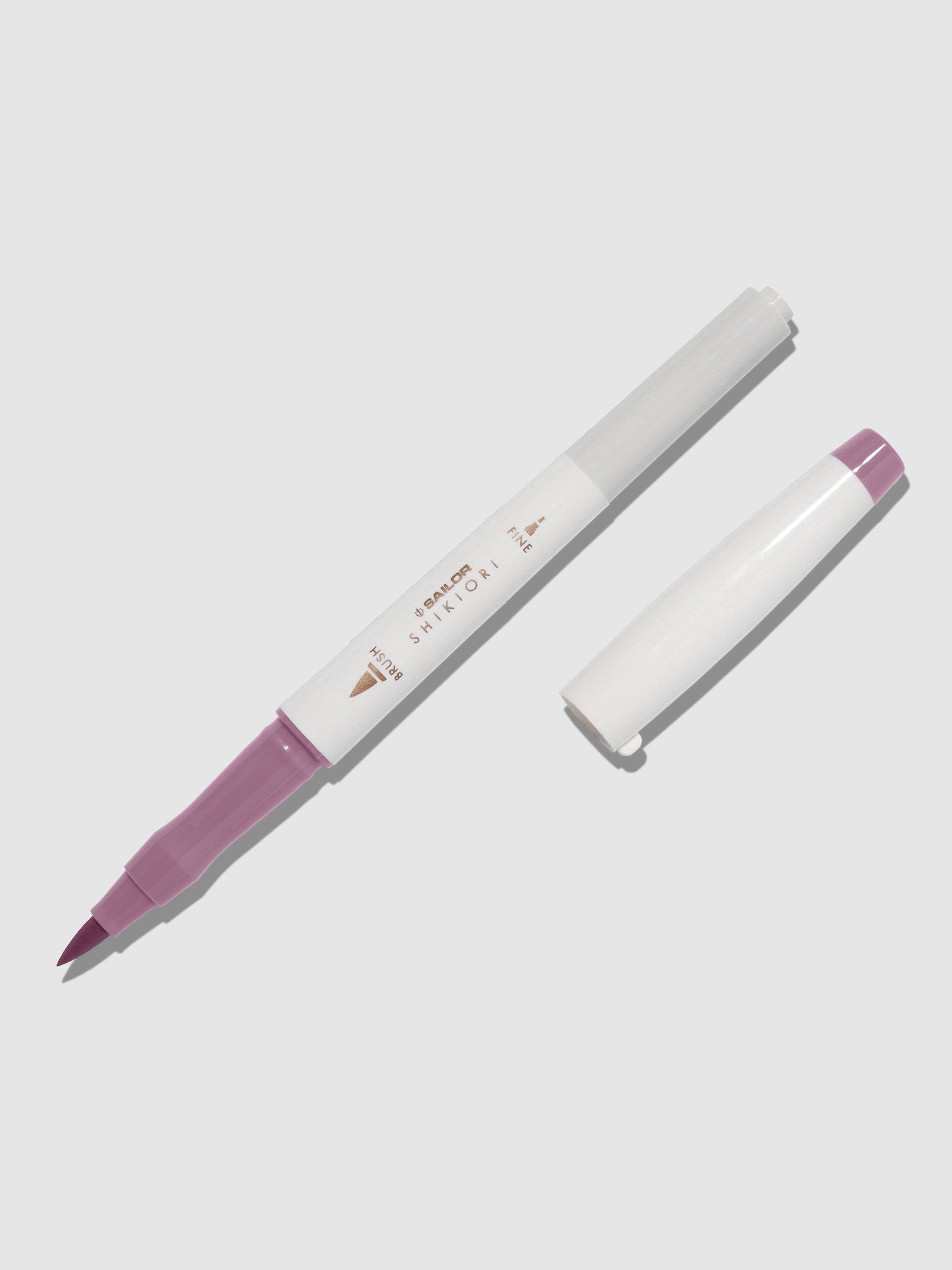 Brush pen displayed on a neutral background. It is uncapped with its brush nib exposed, and the cap lying parallel to the marker. Color pictured is Yozakura.