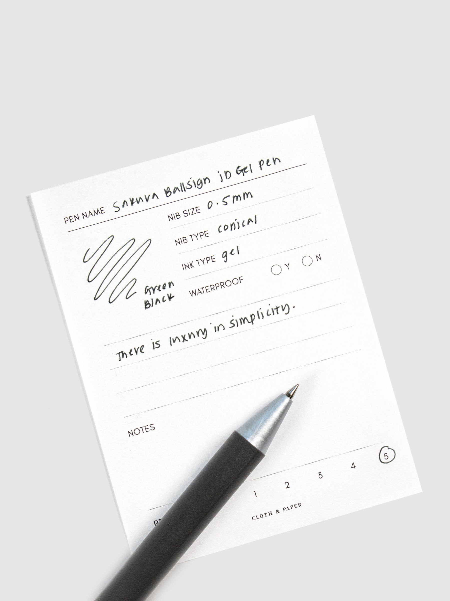 Pen in Green Black resting on a pen test sheet displaying a writing sample detailing the pen's specs.