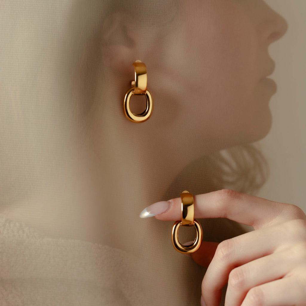 A spoiler from our Aesthete Box for Spring 2024.  A woman is wearing one of The Skatt Earrings from OMA The Label as well as holding one on her finger.