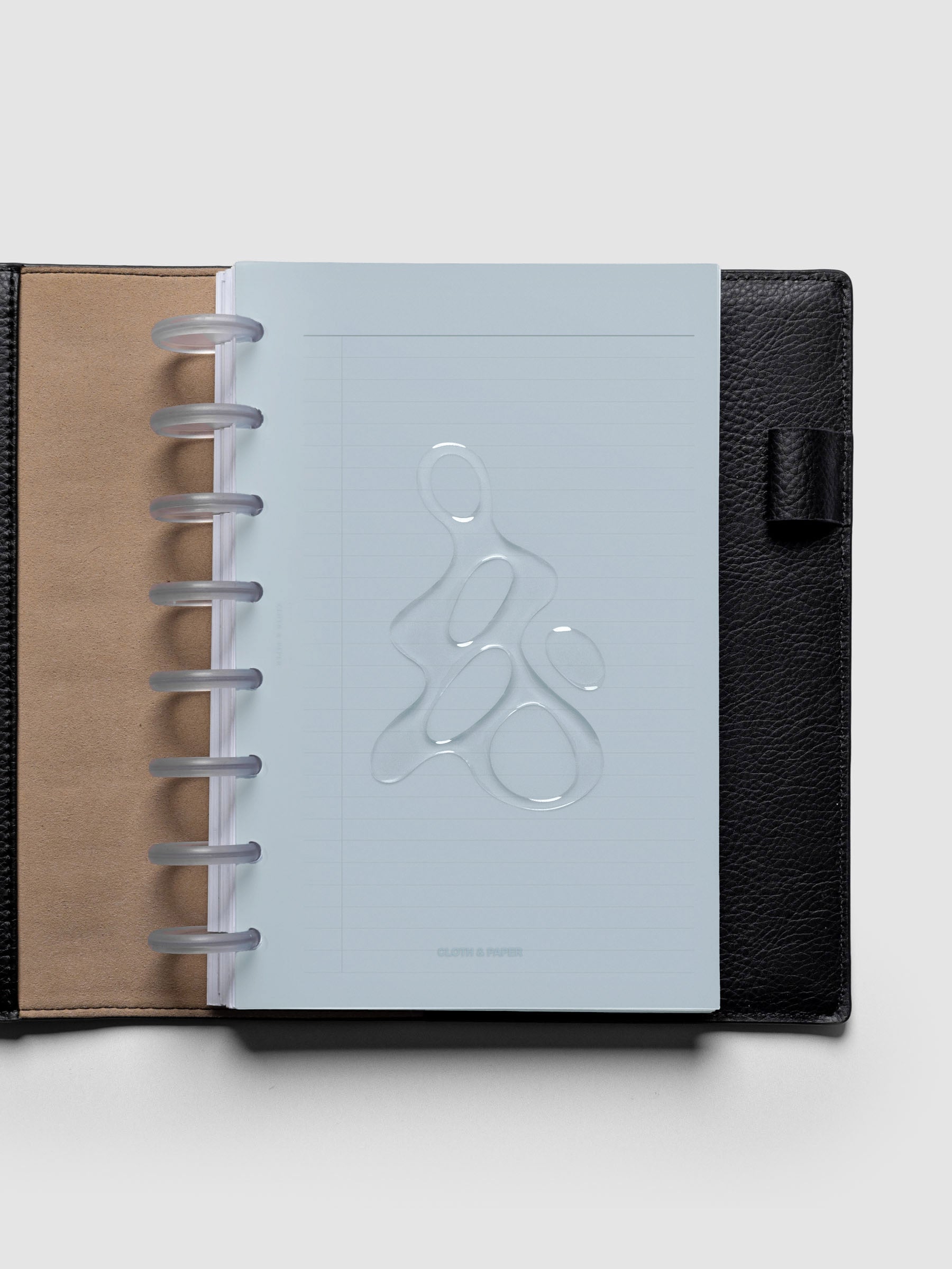 Light blue, semi-transparent, and glossy plastic planner dashboard with organic raised shape design in size Half Letter discbound in a black leather folio.