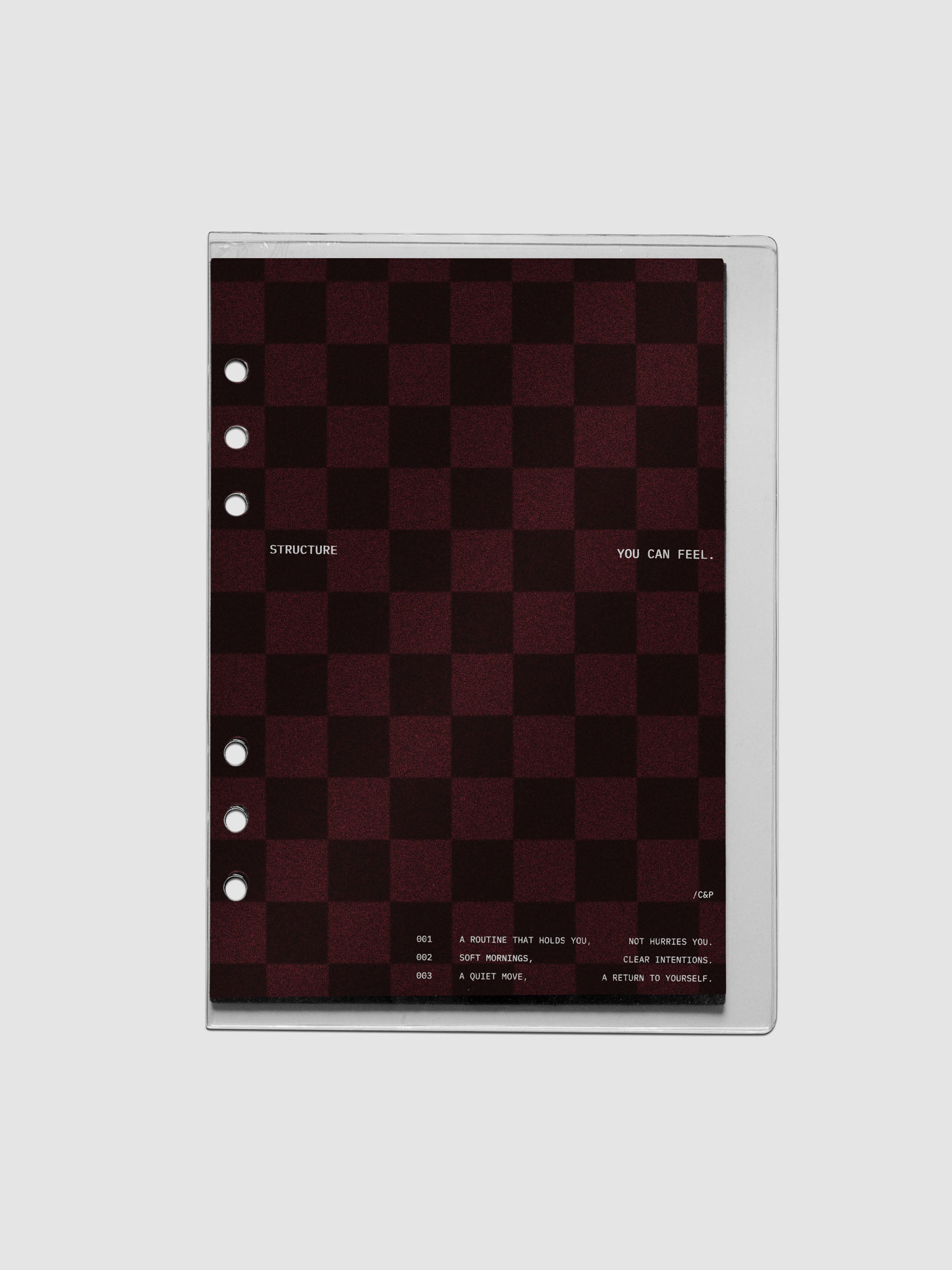 A5 sized velvet checkered dashboard in the color Bordeaux in between two crystal clear plastic planner covers with text printed on the cover on the theme of structure and routines.