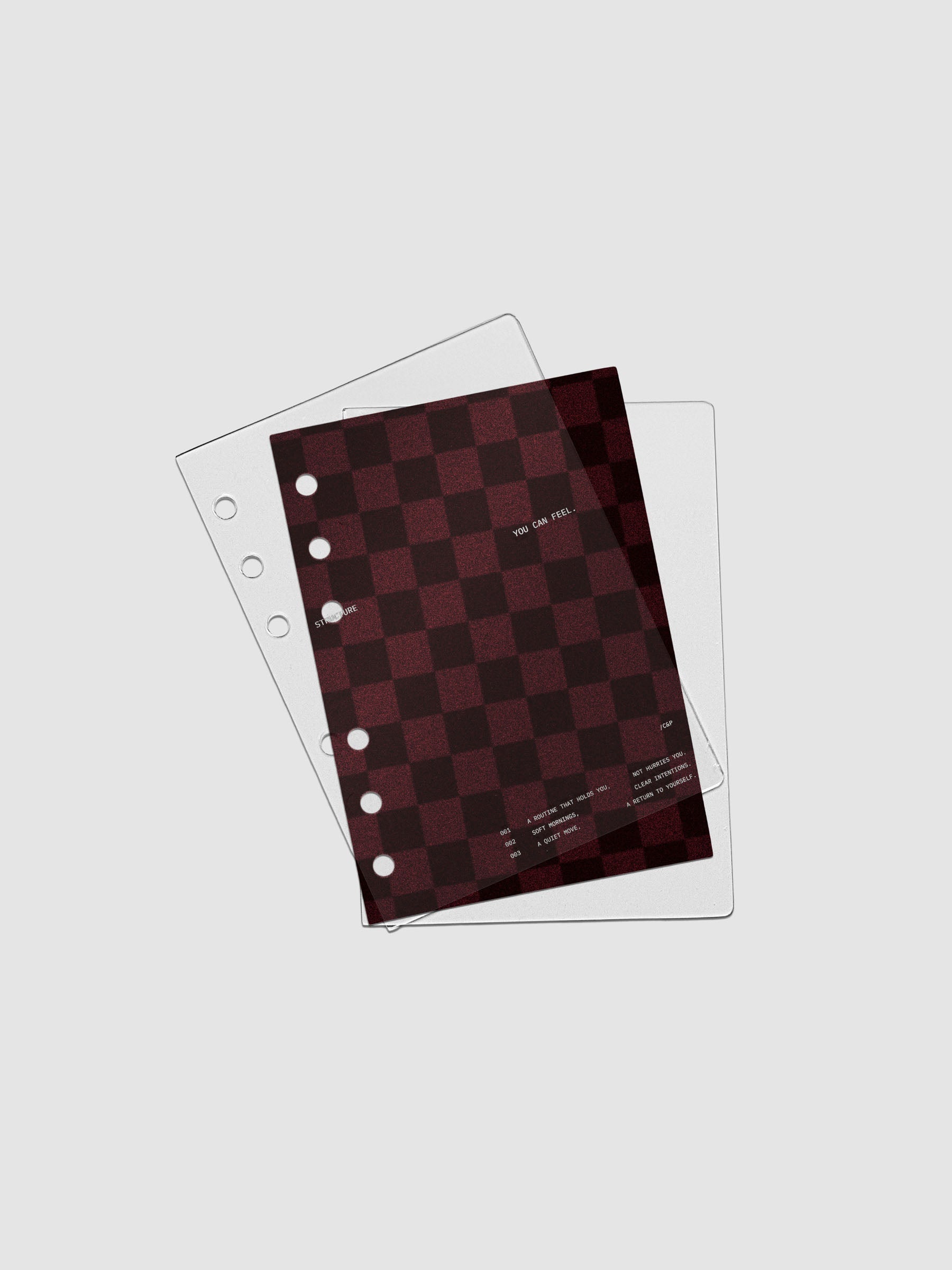 A6 sized velvet checkered dashboard in the color Bordeaux in between two crystal clear plastic planner covers with text printed on the cover on the theme of structure and routines.