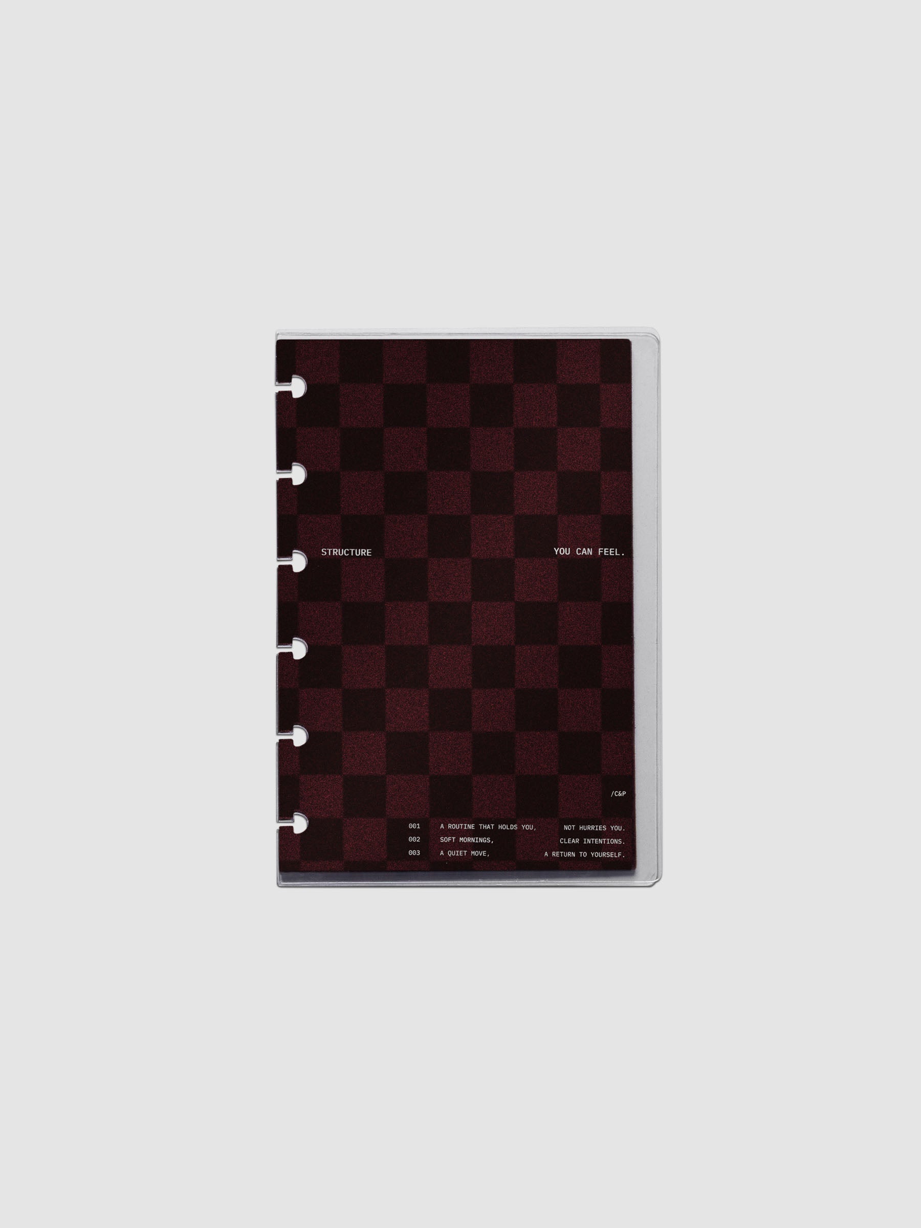 CP Petite sized velvet checkered dashboard in the color Bordeaux in between two crystal clear plastic planner covers with text printed on the cover on the theme of structure and routines.