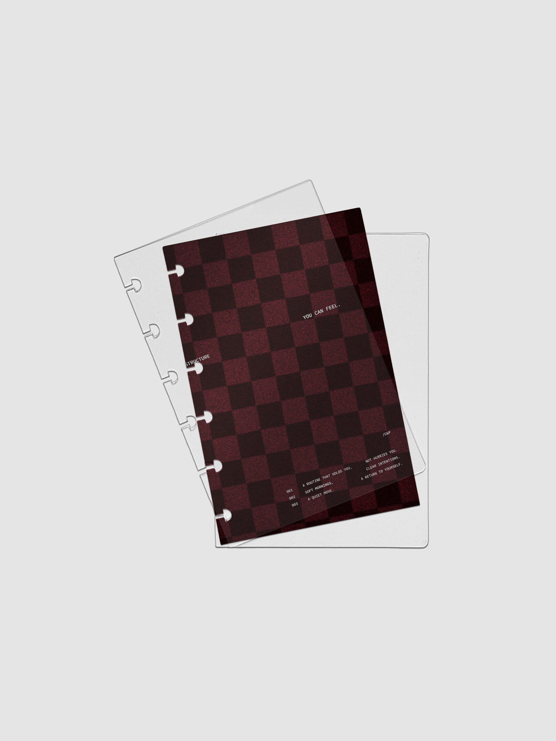 CP Petite sized velvet checkered dashboard in the color Bordeaux in between two crystal clear plastic planner covers with text printed on the cover on the theme of structure and routines.