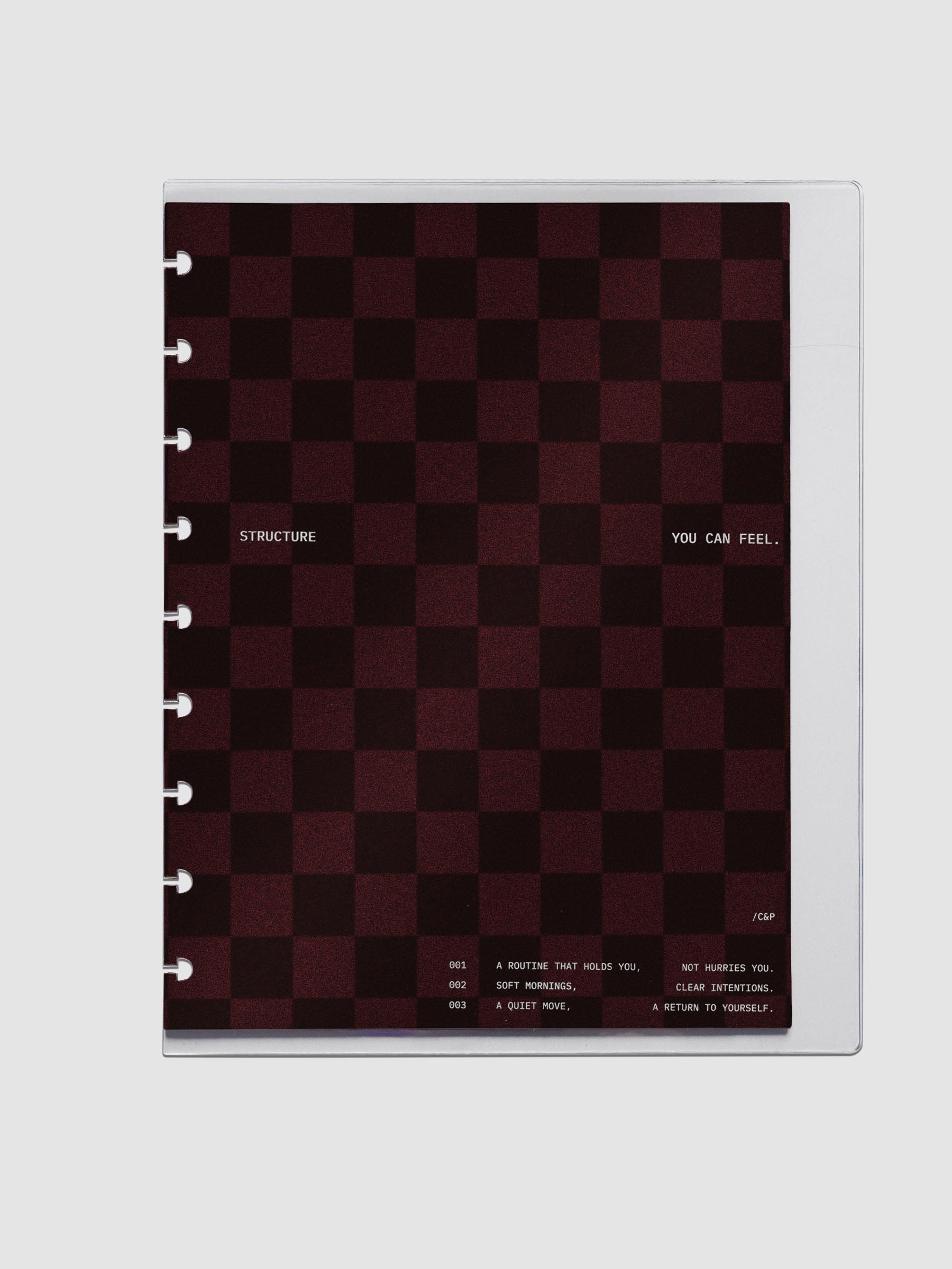 HP Classic sized velvet checkered dashboard in the color Bordeaux in between two crystal clear plastic planner covers with text printed on the cover on the theme of structure and routines.