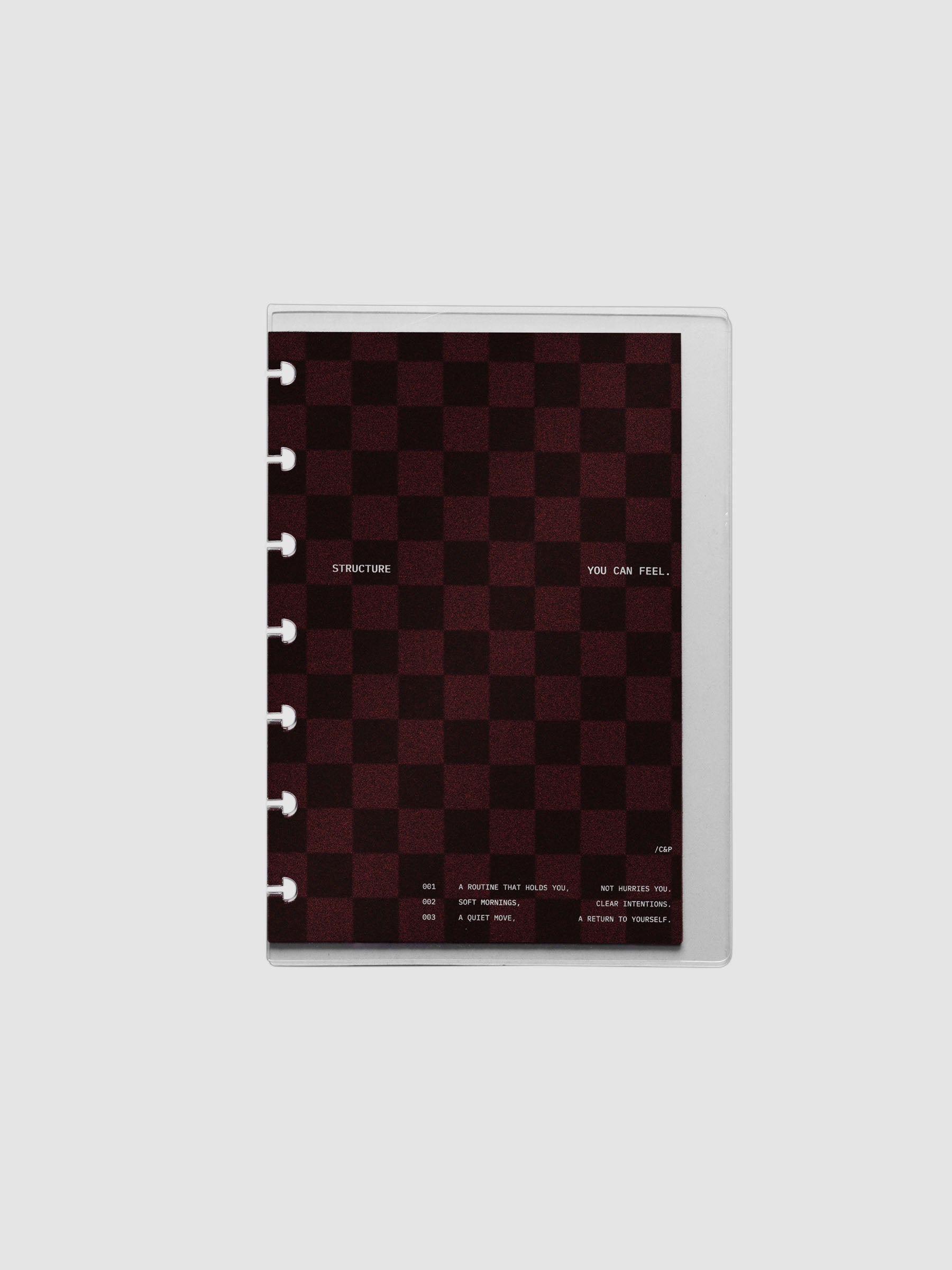 HP Mini sized velvet checkered dashboard in the color Bordeaux in between two crystal clear plastic planner covers with text printed on the cover on the theme of structure and routines.