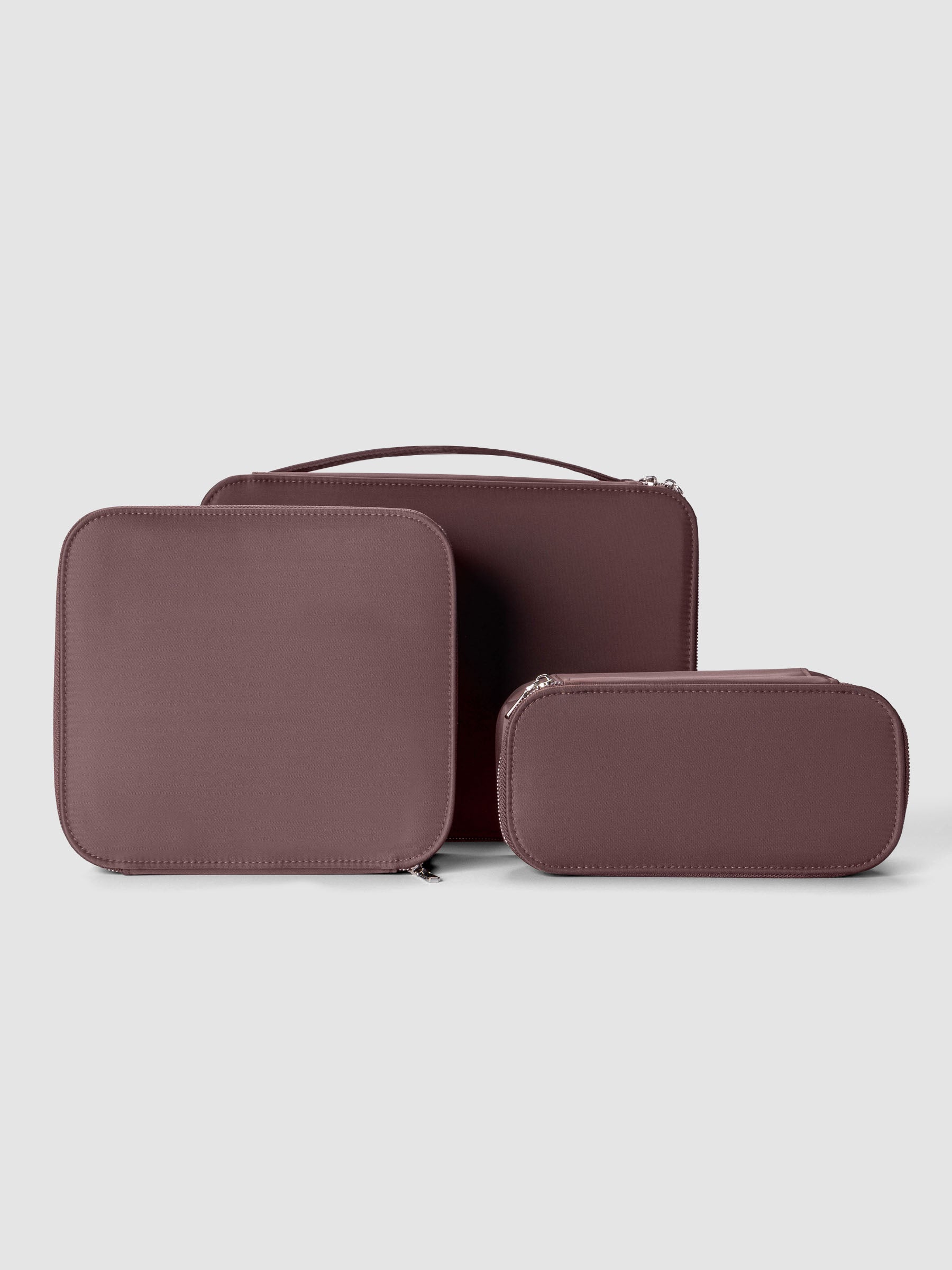 Set of three nesting packing cubes in small, medium, and large in the color walnut on a neutral background.