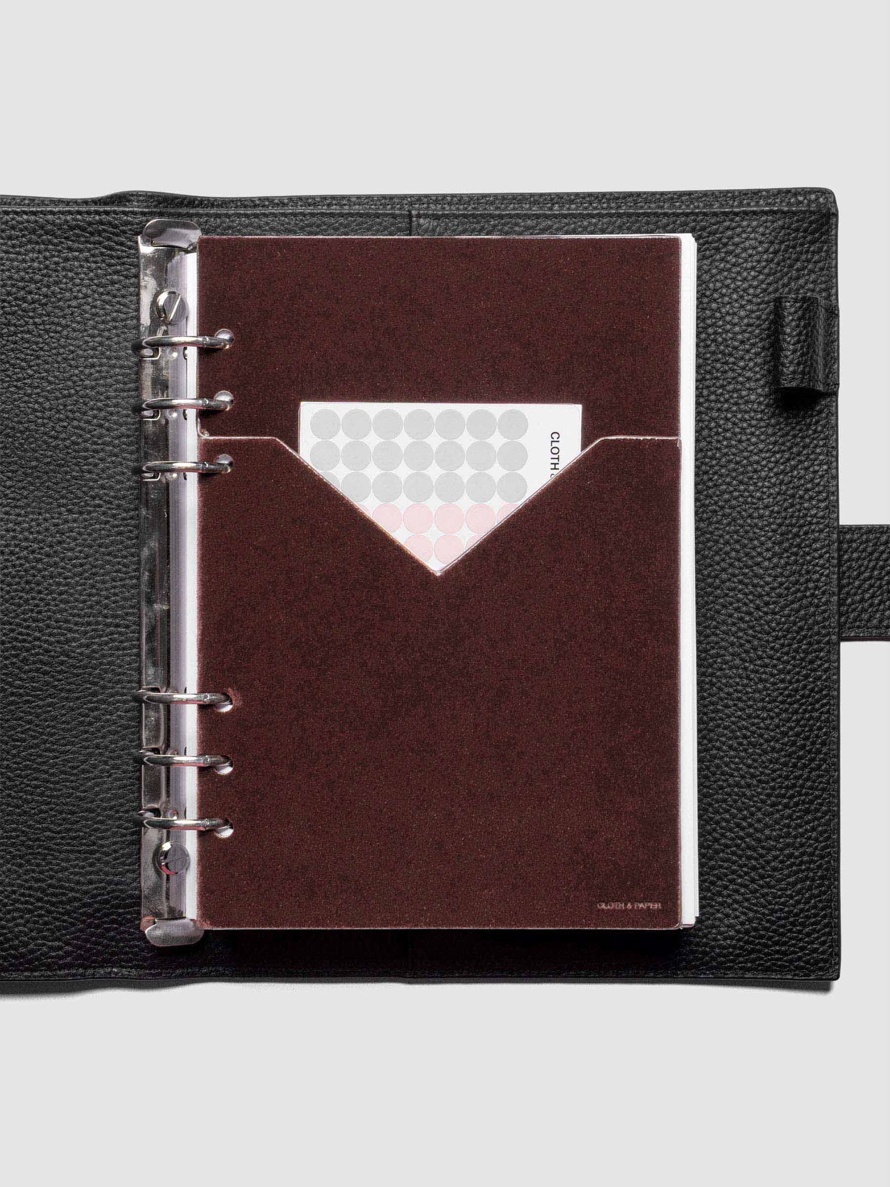Velvet Pocket Folder in Bordeaux pre-punched for A5 planners shown in a black leather agenda with stickers in the pocket.