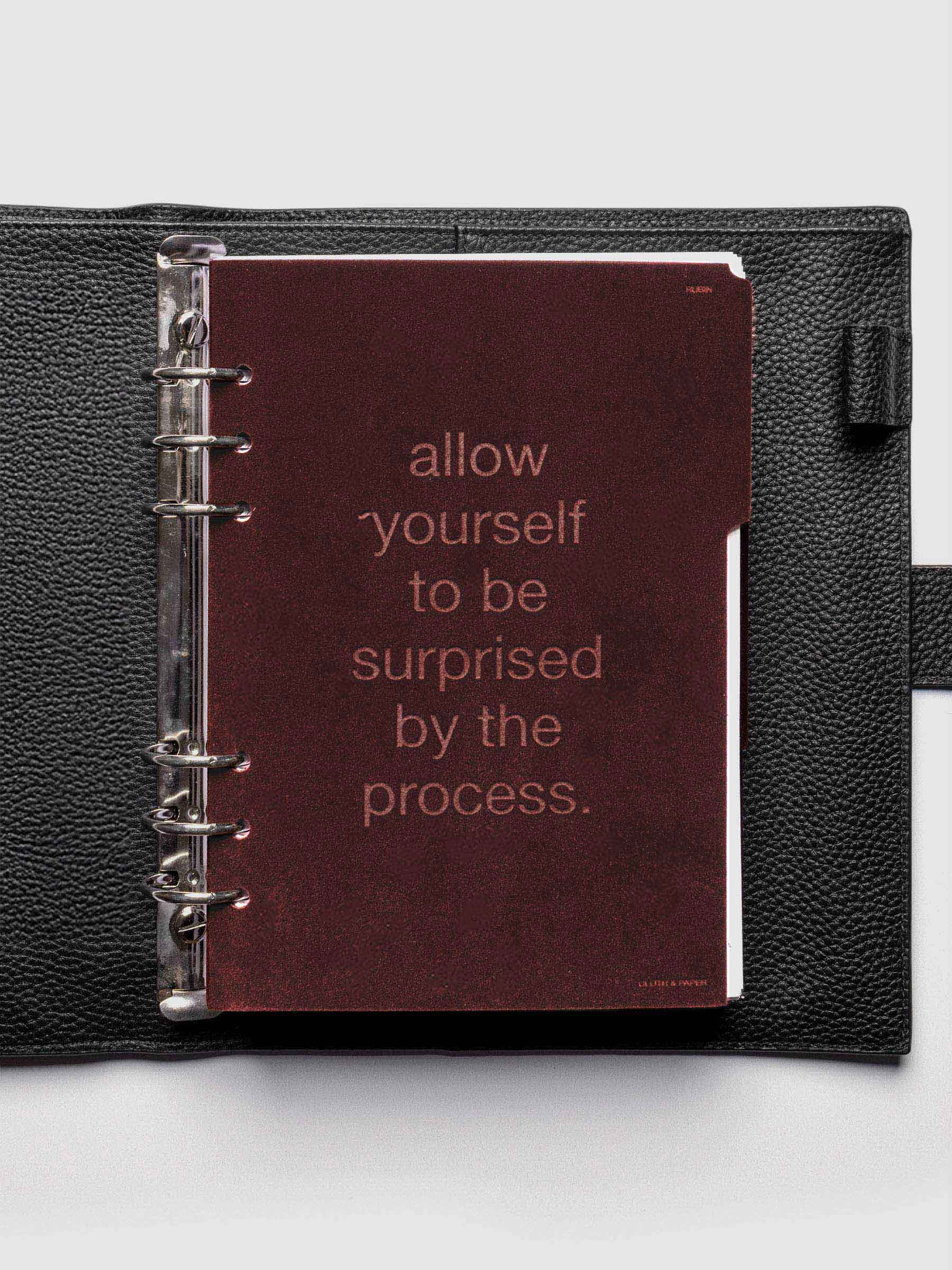 First velvet side tab planners dividers in the color Bordeaux with text deboss design reading "allow yourself to be surprised by the process" in size A5 shown ringbound in a black leather agenda.