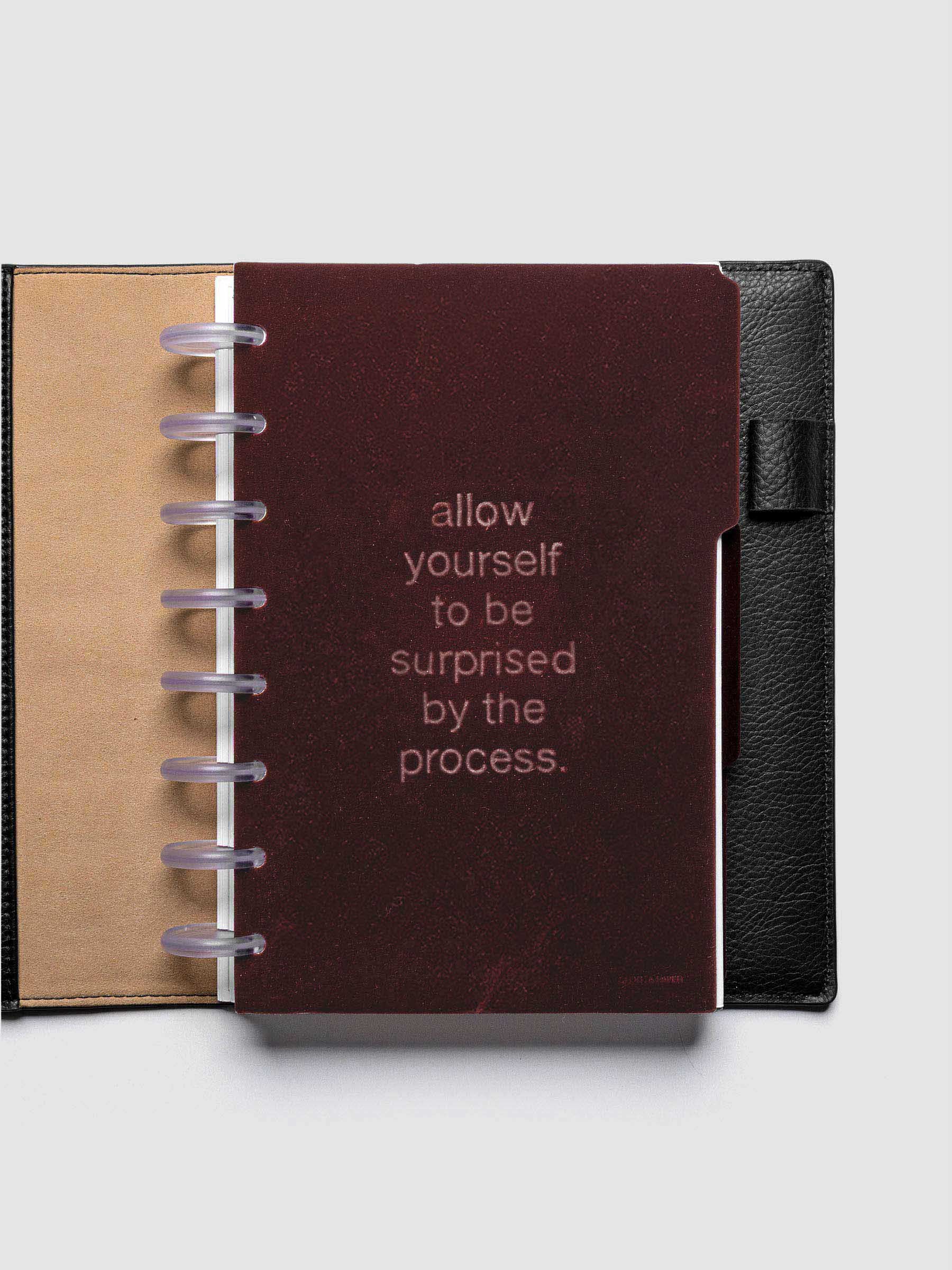 First velvet side tab planners dividers in the color Bordeaux with text deboss design reading "allow yourself to be surprised by the process" in size Half Letter shown discbound in a black leather folio.