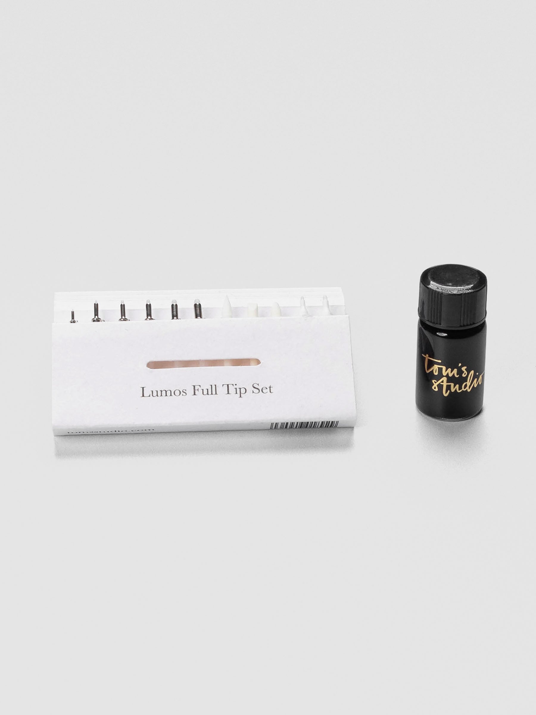 Assortment of Tom’s Studio Lumos Pro interchangeable pen tips displayed beside a refillable ink reservoir on a white surface.